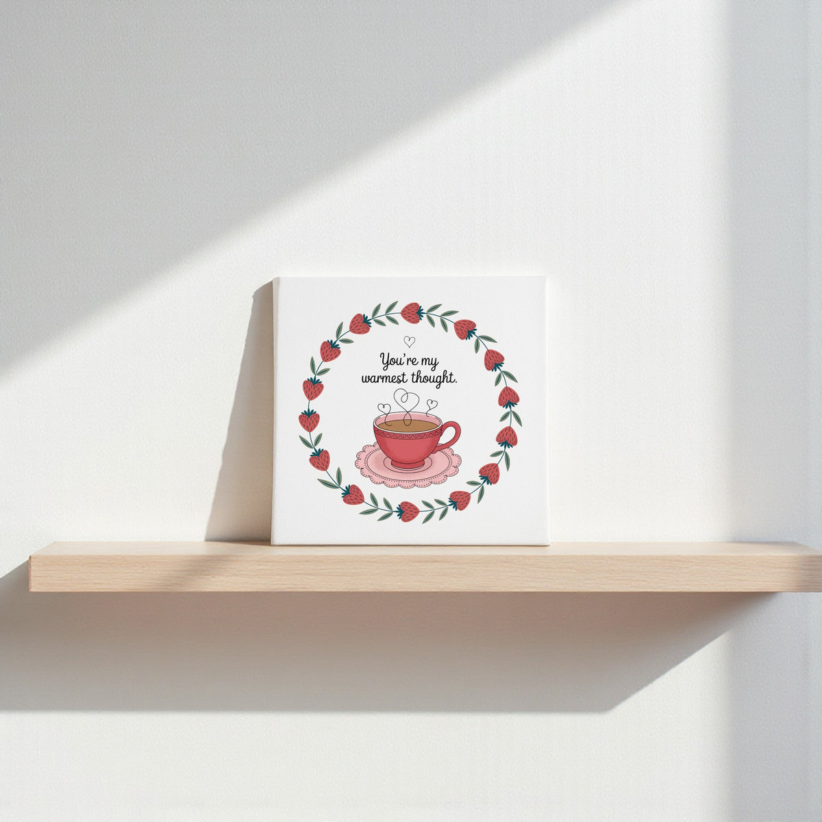 The Warmest Thought Tea-Inspired Canvas Art by Mirabilia Boutique features a red teacup with hearts and a leafy berry wreath, plus “You’re my warmest thought”—a perfect gift for tea lovers or romantic decor.