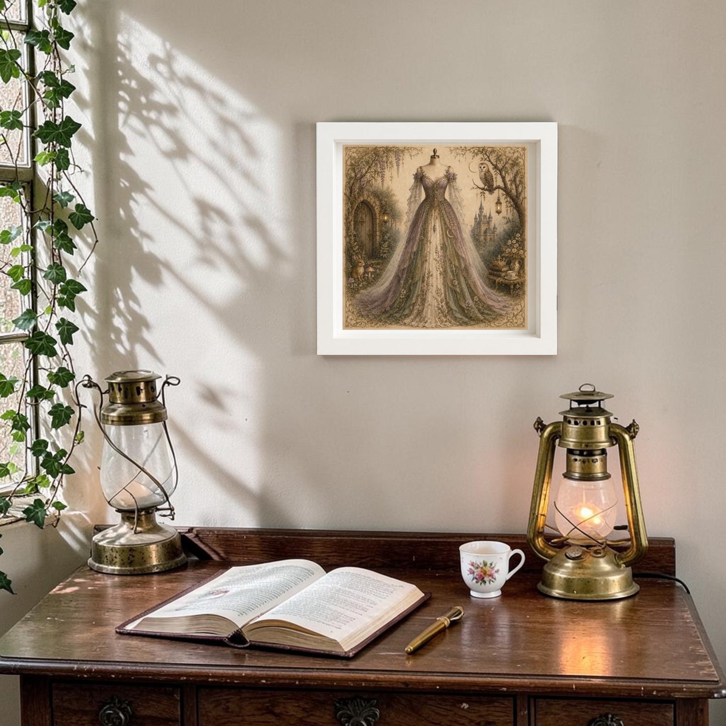 A wooden desk with an open book, pen, floral teacup, and two vintage lanterns sits beneath a sunlit window where ivy trails along the sill. On the beige wall above, Wisteria Dreams | Curated Couture Artwork by Mirabilia Boutique brings a touch of elegance to this enchanted hollow.