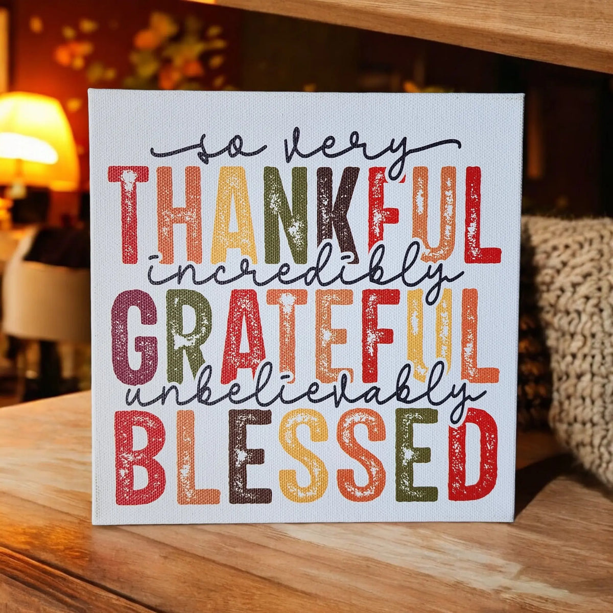 The Mirabilia Boutique’s Thankful Grateful Blessed Inspirational Sign for Seasonal Home Decor showcases the words "So Very Thankful, Incredibly Grateful, Unbelievably Blessed" in vibrant, textured letters. Its background depicts a cozy, warmly lit room with a lamp, chair, and blurred decorations in inviting Thanksgiving hues. Ideal for enhancing your home decor!