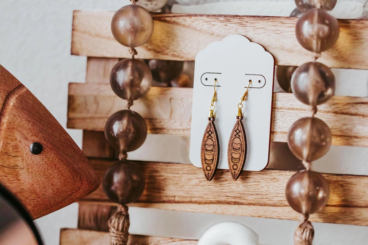Kayak Earrings by Mirabilia Boutique—laser-cut wooden dangle earrings displayed on a white card, surrounded by brown beads and wood decor. Perfect canoe gift for river girls, paddlers, or any outdoor lover.