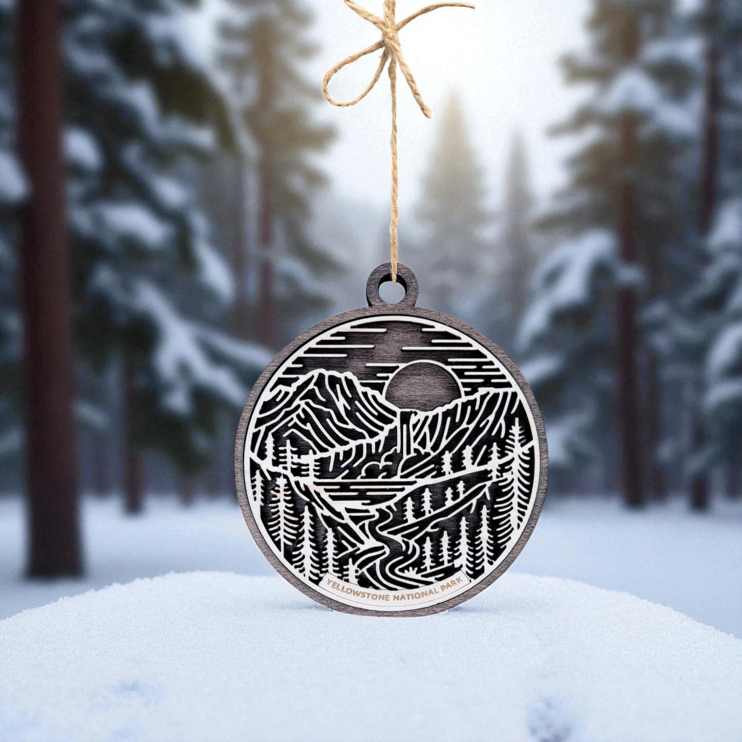The Yellowstone National Park Ornament by Mirabilia Boutique is a handcrafted wooden decoration featuring an engraved mountain, tree, and river scene—perfect rustic holiday decor for nature lovers.
