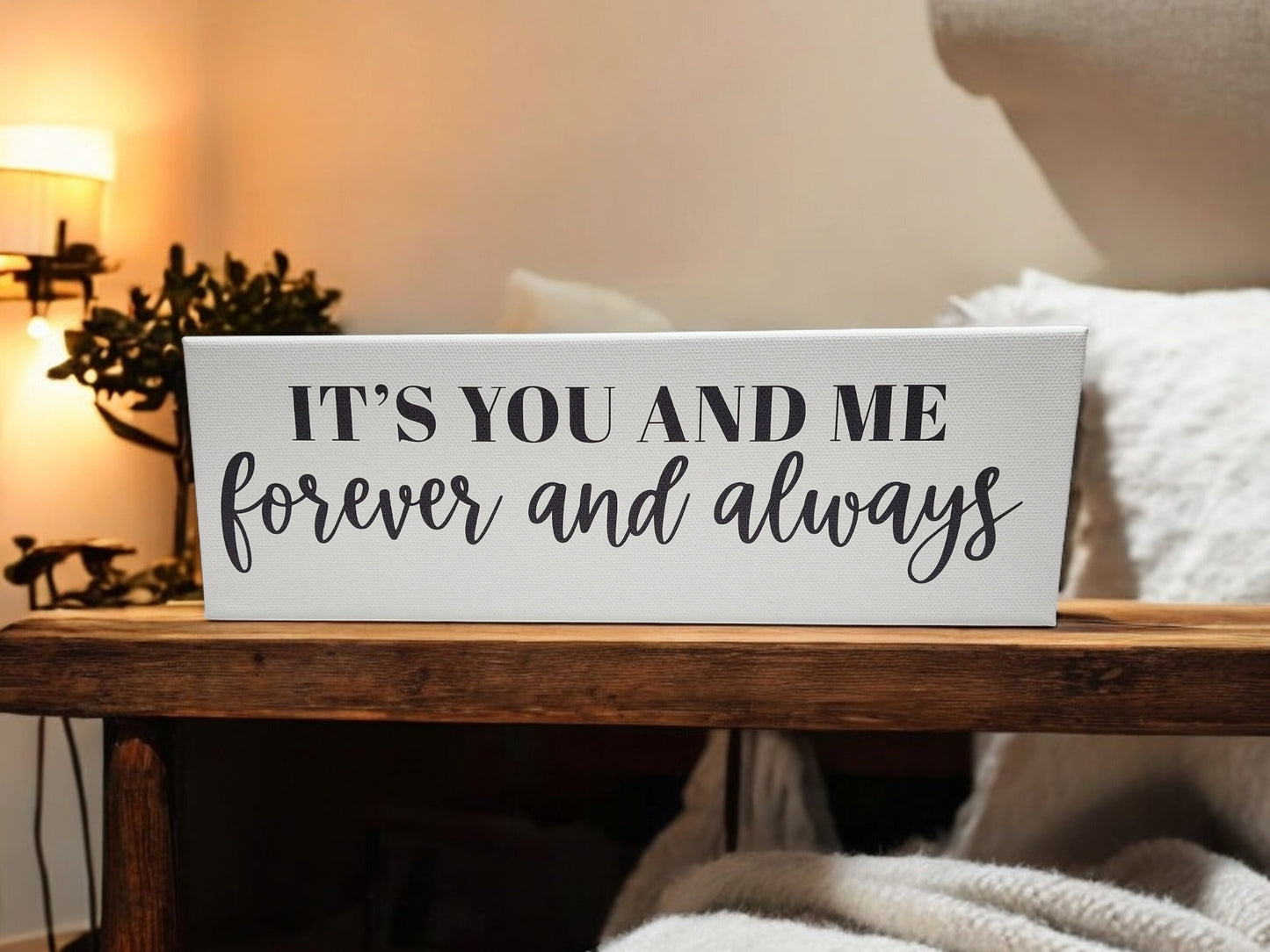 The Mirabilia Boutique "It’s You and Me Always and Forever" 4x12 canvas shelf sitter makes charming couple’s decor, featuring a romantic love quote—shown on a wooden table with cozy accents for added ambiance.