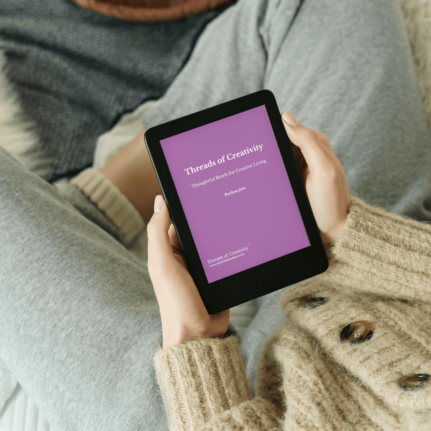 A person in cozy clothes holds an e-reader displaying the cover of "Threads of Creativity" by Barbara Jade, with a purple background and white text.