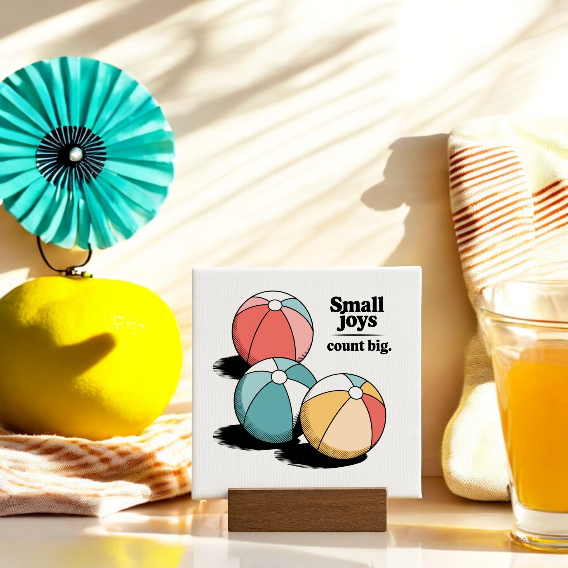 The Mirabilia Boutique Small Joys Count Big Mini Canvas – 4x4 Summer Desk Sign features three colorful beach balls and uplifting words on a wooden base, perfect for bright summer décor in any sunlit space.