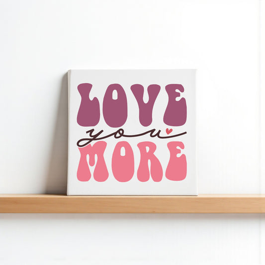 The Love You More 8x8 Canvas by Mirabilia Boutique features bold pink and purple retro letters with a heart over the "u" on a white background, adding playful Valentine charm to any shelf or wall.