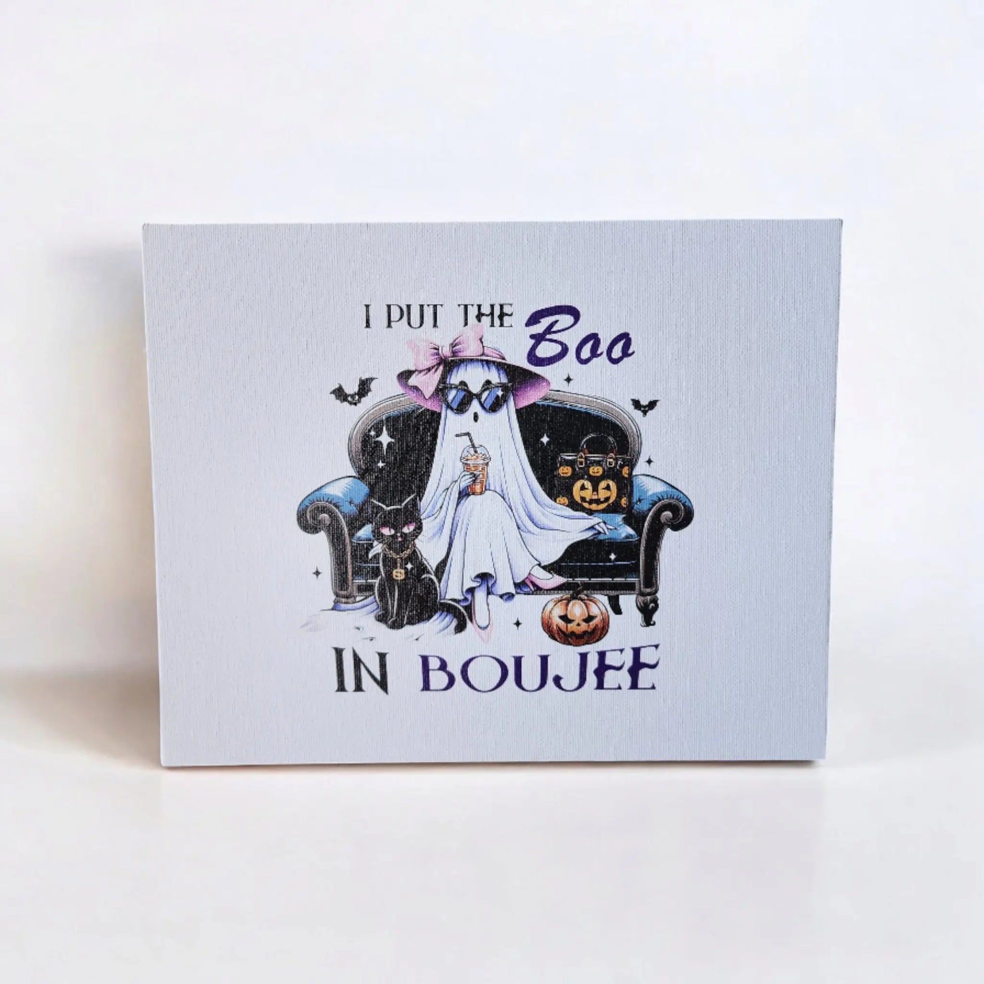 The Funny Halloween Sign: "I put the Boo in Boujee" by Mirabilia Boutique is a captivating wall art piece on a canvas panel. It features a stylish ghost wearing sunglasses and a witch hat, lounging on a fancy couch accompanied by two black cats, surrounded by a spider, bats, and pumpkins. The background is plain white with the playful text above and below declaring "I put the Boo in Boujee." Perfect for Halloween decor or any ghost enthusiast!