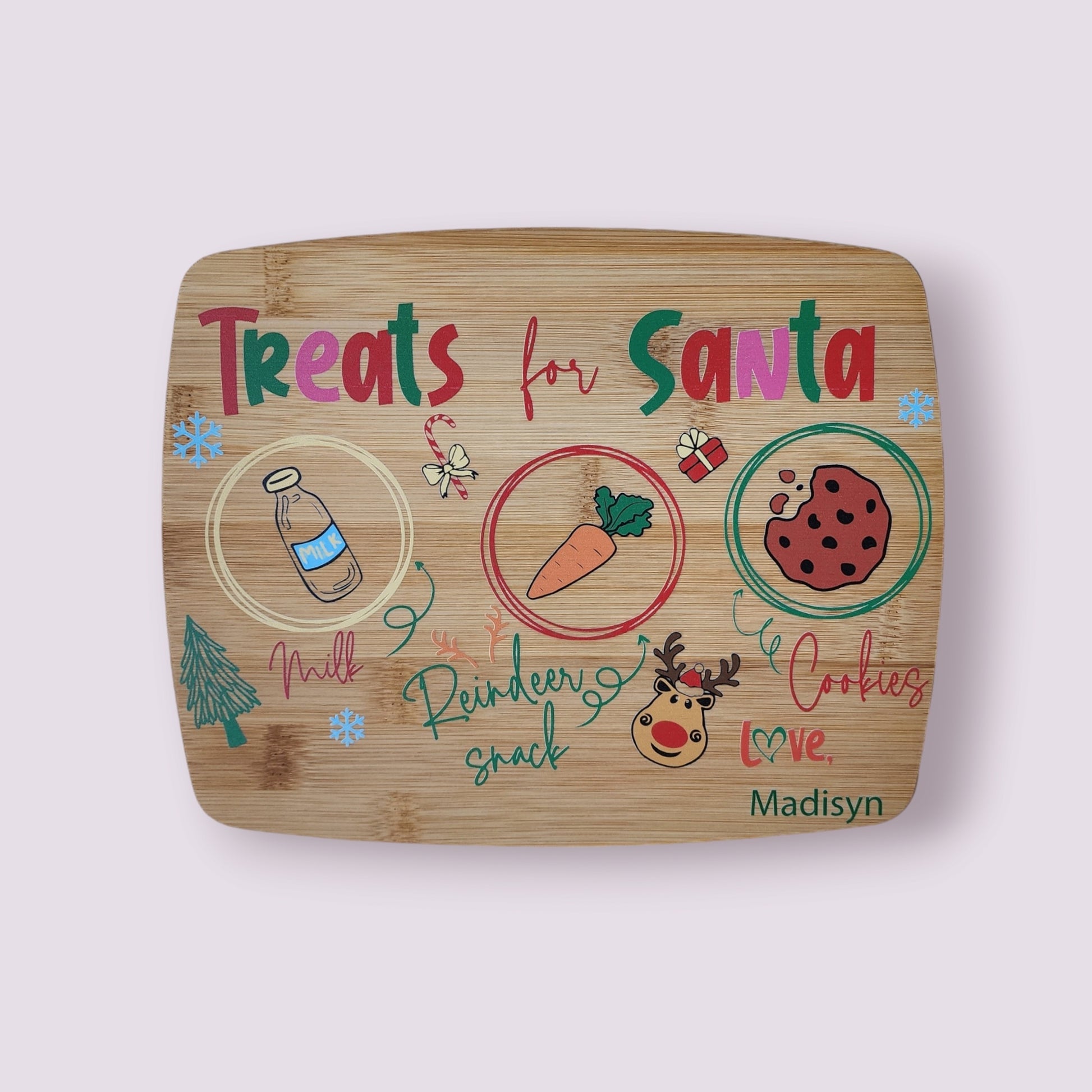 The Santa Cookie Board Personalized from Mirabilia Boutique is a charming addition to the Christmas Eve tradition. Featuring colorful drawings of a milk bottle, carrot, and cookie with "Treats for Santa" written on it, it is adorned with delightful decorations including a reindeer, gift, and snowflakes. The name "Madisyn" is hand-written at the bottom for that extra personal touch.