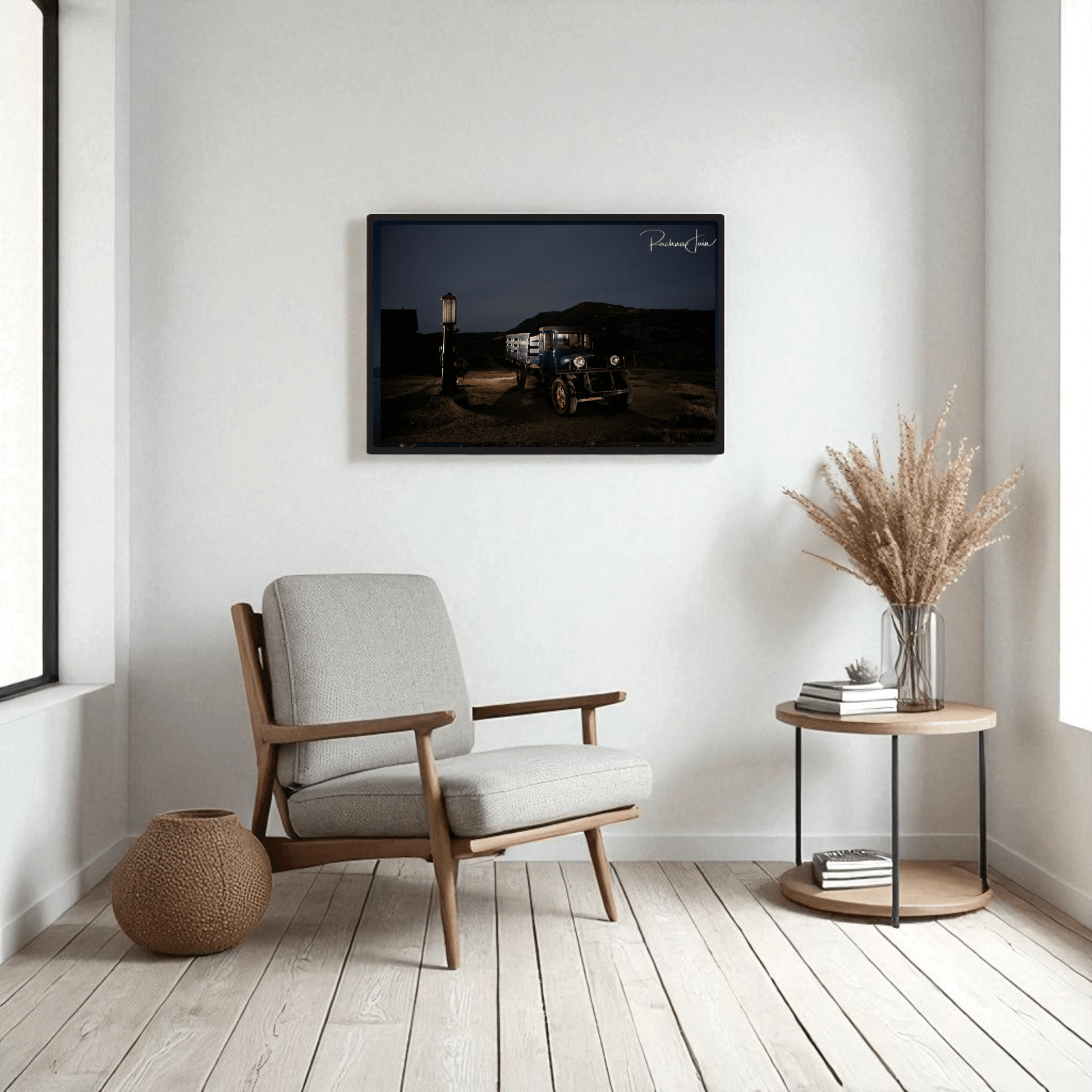 A cozy modern living room with a light gray armchair, small round table with vase, woven basket, and Mirabilia Boutique’s “Abandoned Truck at Bodie State Park” light‑painted art print hanging on a white wall.