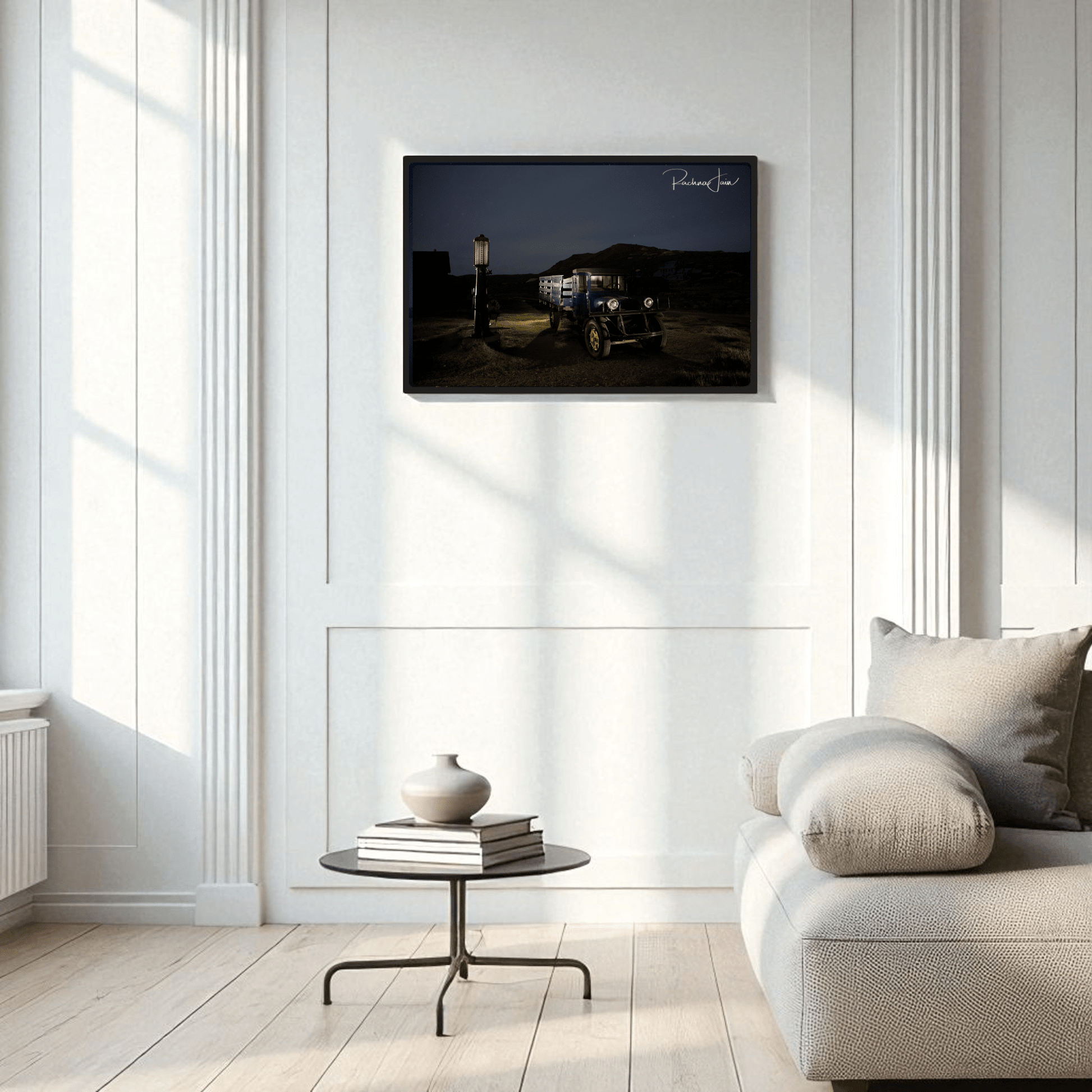 A modern, minimalist living room with white walls, a light gray sofa, a round glass coffee table, and Mirabilia Boutique’s "Abandoned Truck at Bodie State Park | Light‑Painted Art Print" framed on the wall.