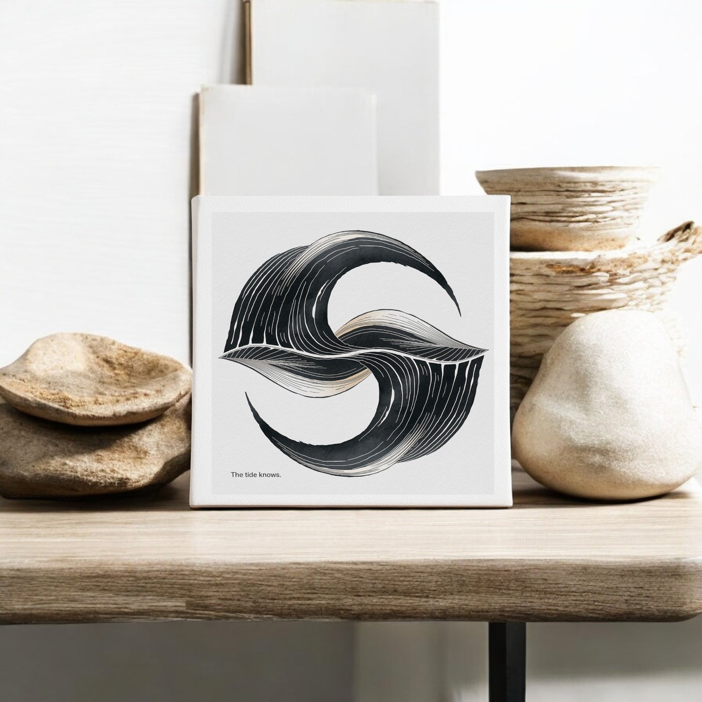 The Tide Knows Canvas – 8x8 Abstract Coastal Wall Art by Mirabilia Boutique features black wave designs and the phrase “The tide knows.” Perfect minimalist decor for meditation rooms, shown on wood with stones and textured bowls.