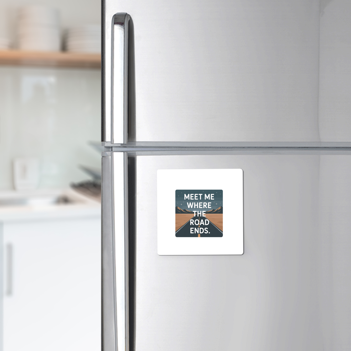 A silver fridge features the Mirabilia Boutique "Meet Me Where the Road Ends Magnet," a square design with a scenic road and bold text—ideal as camper decor or a unique road trip gift for any modern kitchen.