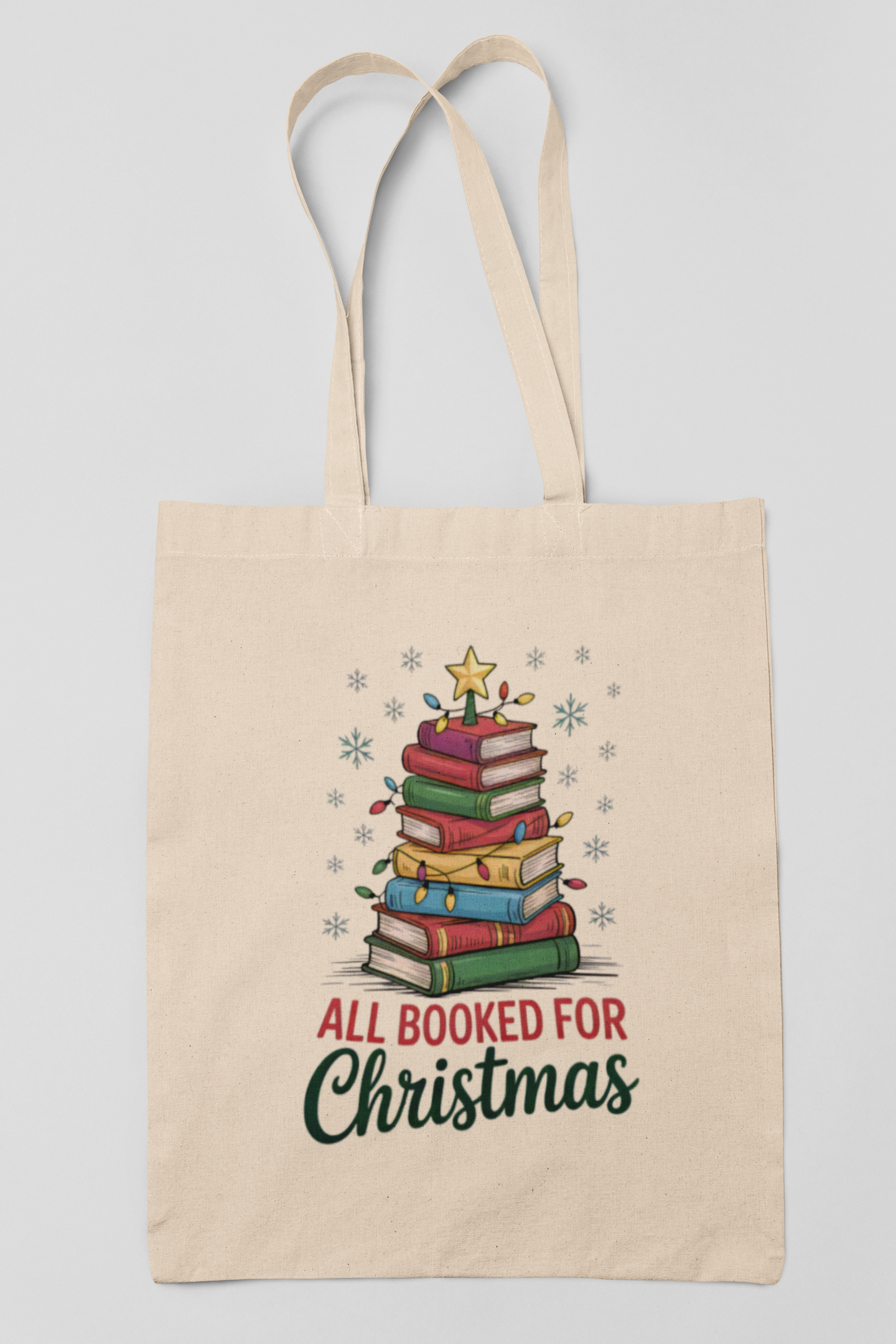 The All Booked for Christmas Book Stack Tote Bag by Mirabilia Boutique features a festive stack of colorful books as a Christmas tree with lights, star, and snowflakes. “All Booked For Christmas” text makes it the perfect gift for any book lover.