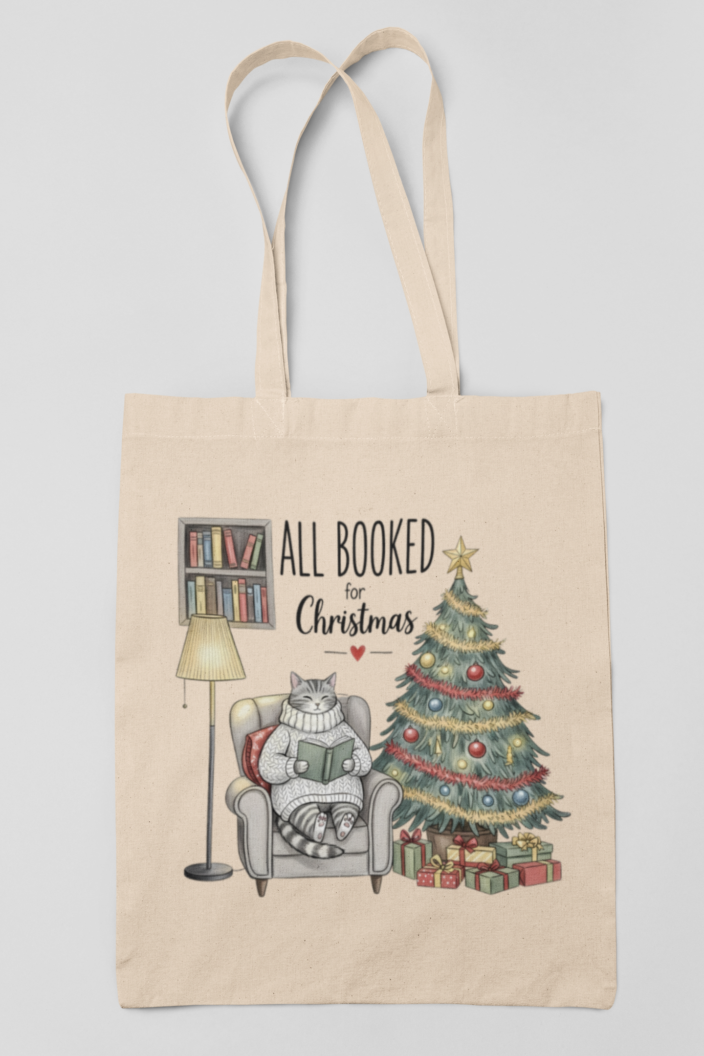 The All Booked for Christmas Cat Tote Bag by Mirabilia Boutique is a beige holiday tote featuring a cat reading by a festive bookshelf and tree, with "All Booked for Christmas" above—an ideal Christmas gift for book lovers.