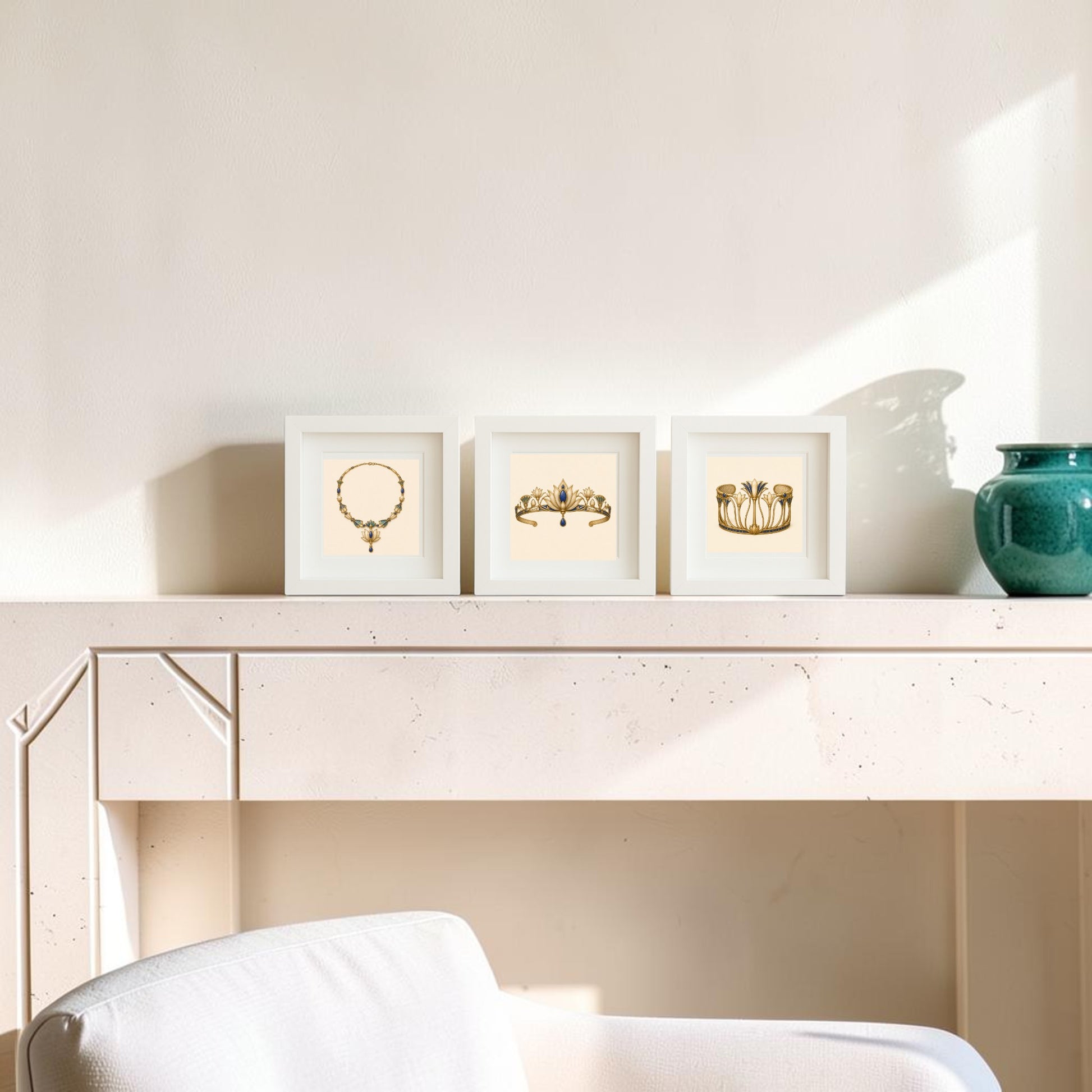 Three framed gold jewelry art prints from the “Adornments of the Nile | Mirabilia Relics” collection by Mirabilia Boutique sit on a beige mantel next to a green vase. Sunlight casts shadows on the light wall behind, and part of a white upholstered chair is visible in the foreground.