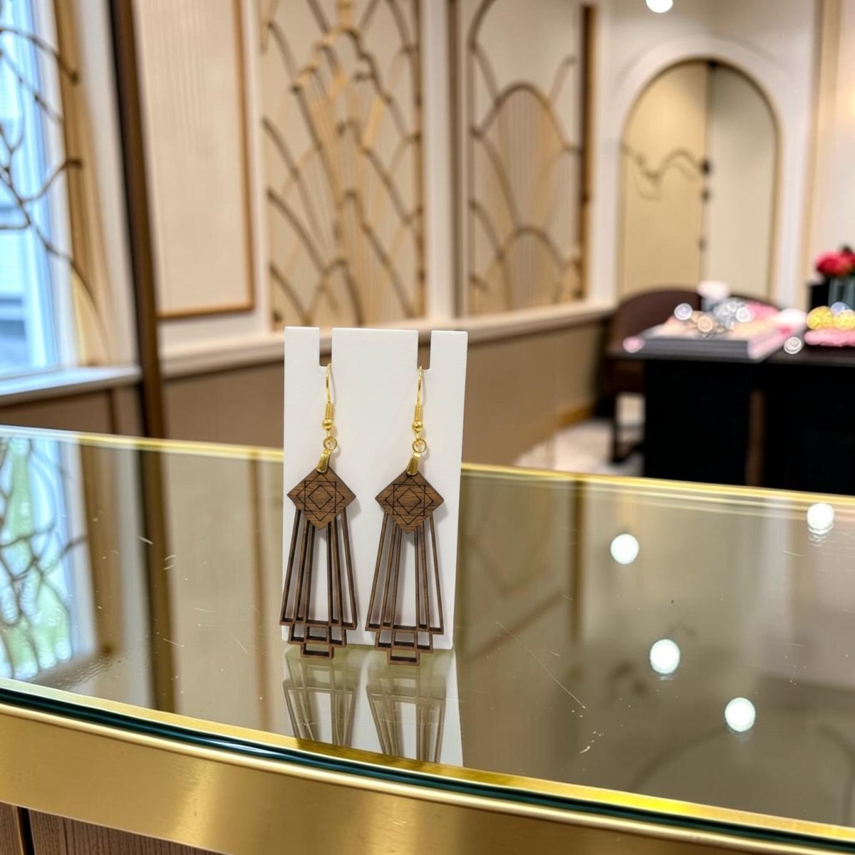 Art Deco Skyscraper Wood Statement Earrings by Mirabilia Boutique with gold hooks, displayed on a white card atop a glass counter in a chic, art deco-inspired jewelry store interior.