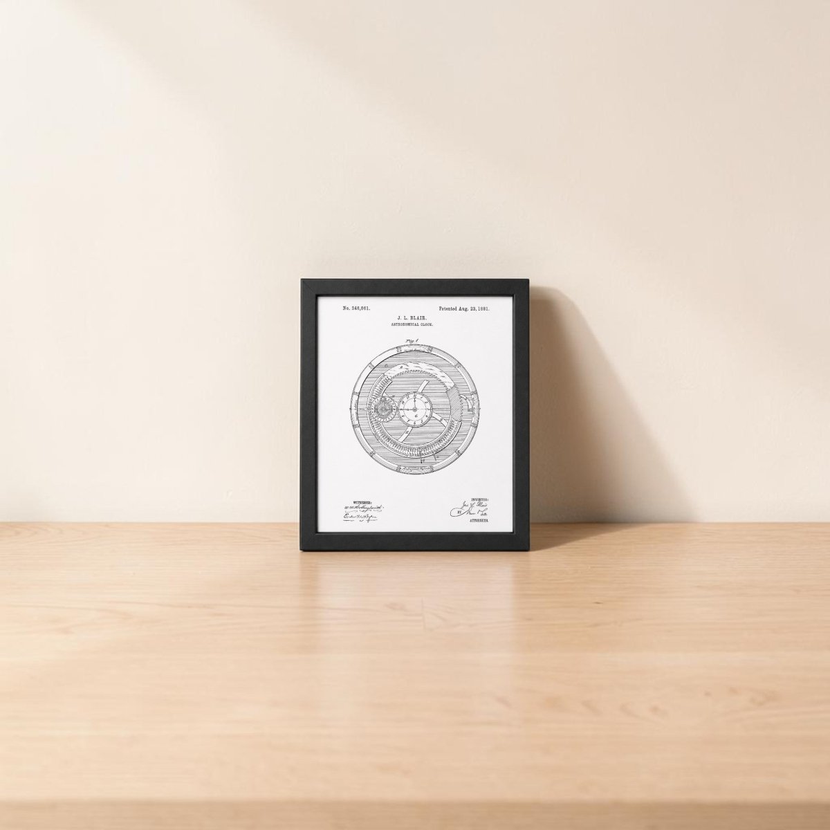 The Astronomical Clock Patent Art Print by Mirabilia Boutique sits framed on a light wooden surface against a beige wall. The tabletop is empty except for the black-and-white vintage-style diagram featured in the print.
