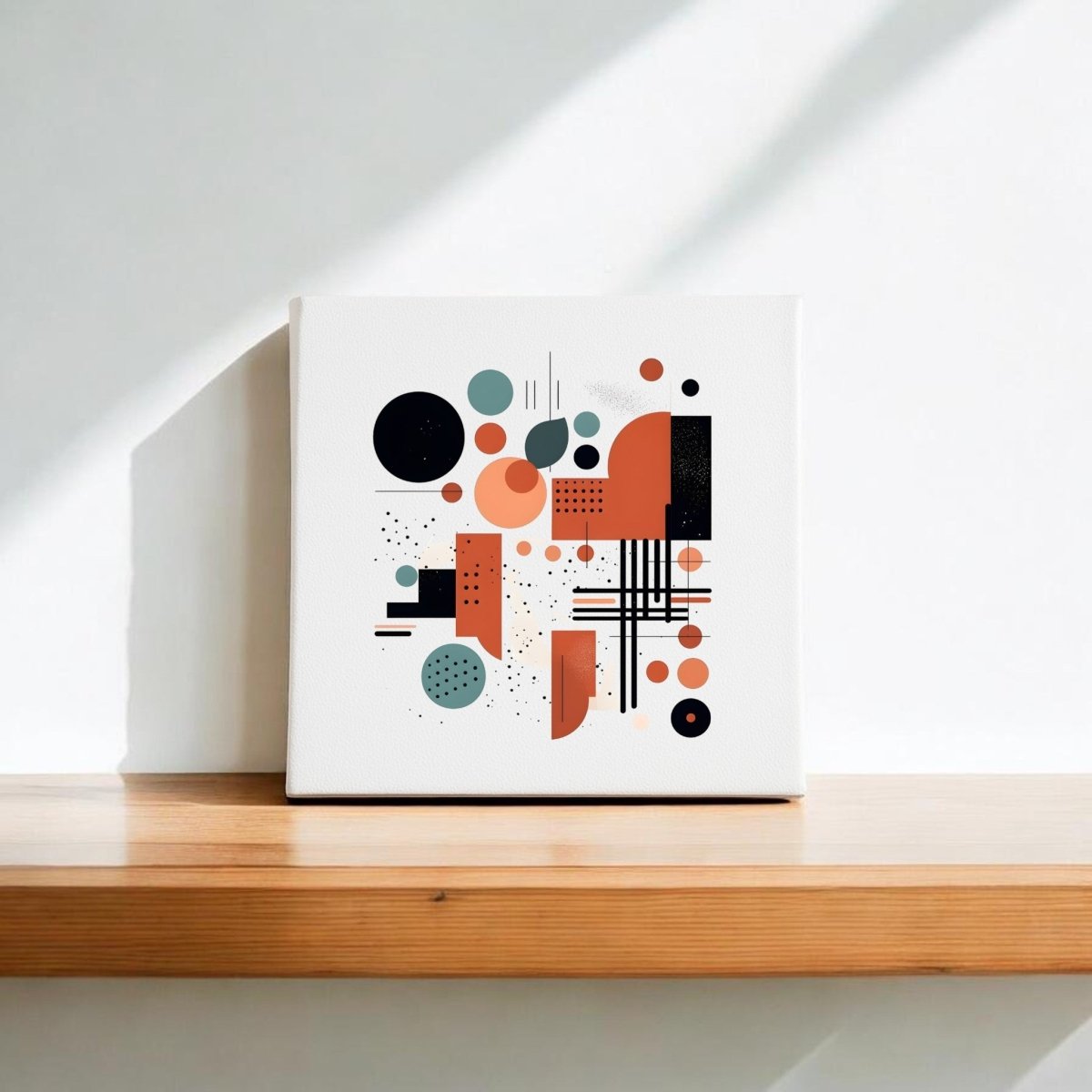 The Atomic Sunrise Mid Century Modern Canvas by Mirabilia Boutique features a geometric abstract design in black, orange, and teal, displayed on a wooden shelf with sunlight casting shadows on the white wall behind.