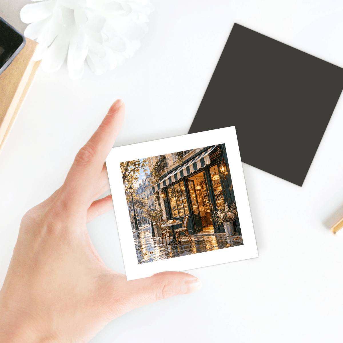 A hand holds a square decorative hardboard The City Before Nine Magnet | Paris Toujours, featuring an image of a Parisian café at dawn.