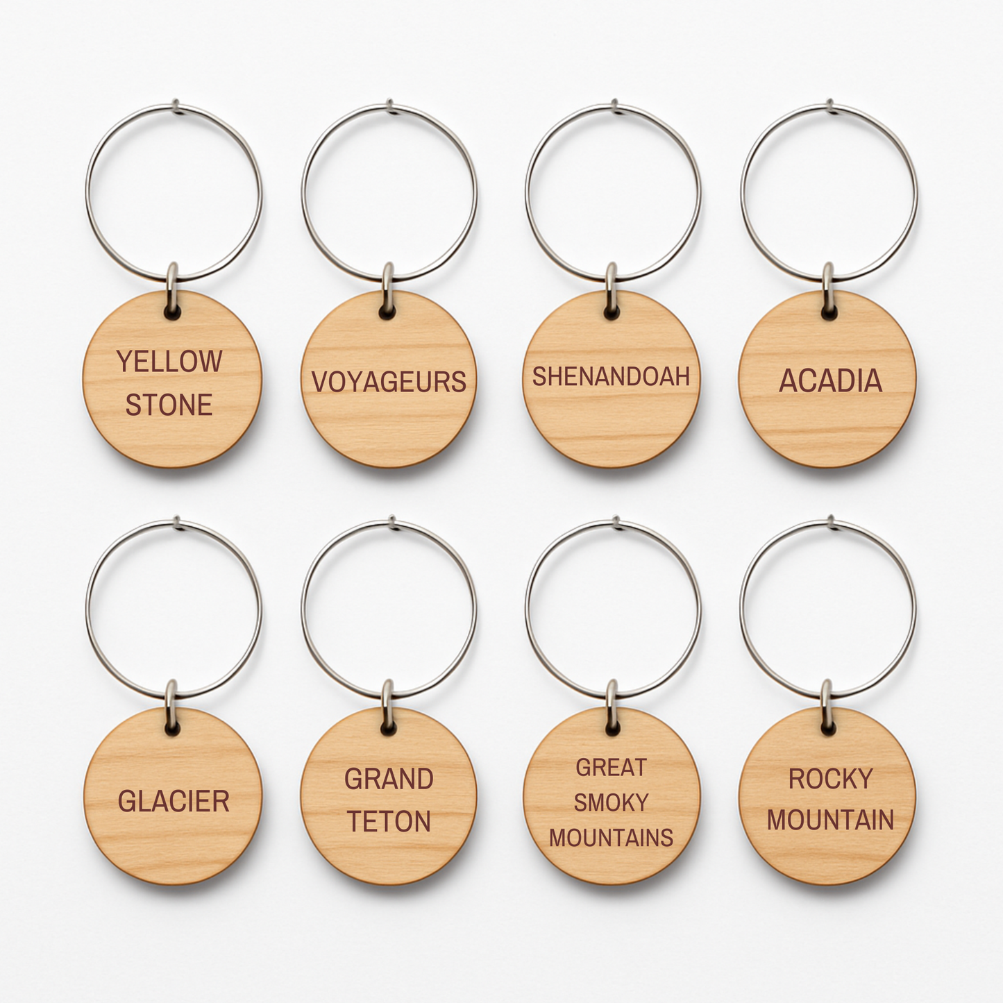 Mirabilia Boutique's Autumn Lodge National Parks Wine Charms feature eight round wooden keychains with metal rings, each engraved with a U.S. national park—perfect rustic accents for your fall gatherings.