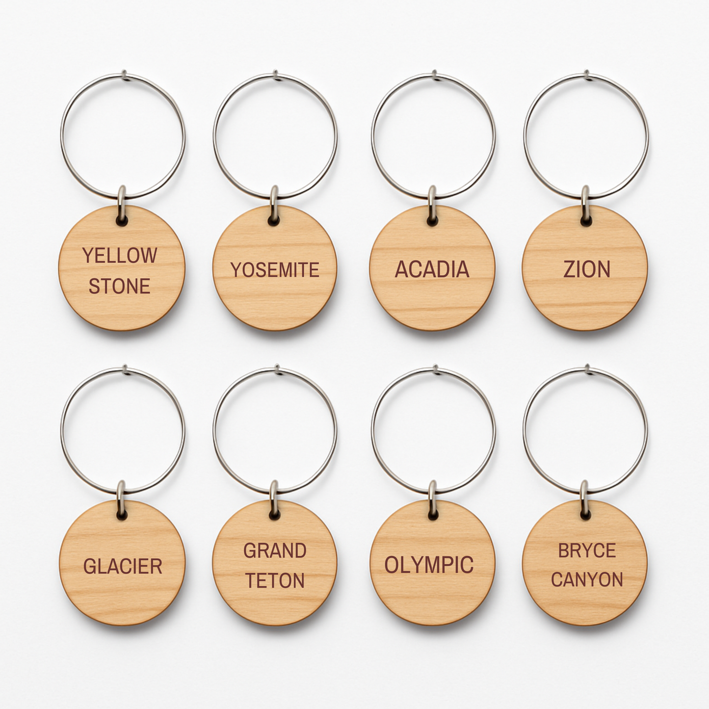 Eight round wooden keychains from Mirabilia Boutique's Awe-Inspiring National Parks Wine Charms are arranged in two rows, each engraved with a U.S. national park name—perfect for outdoor entertaining or as unique wine charms.