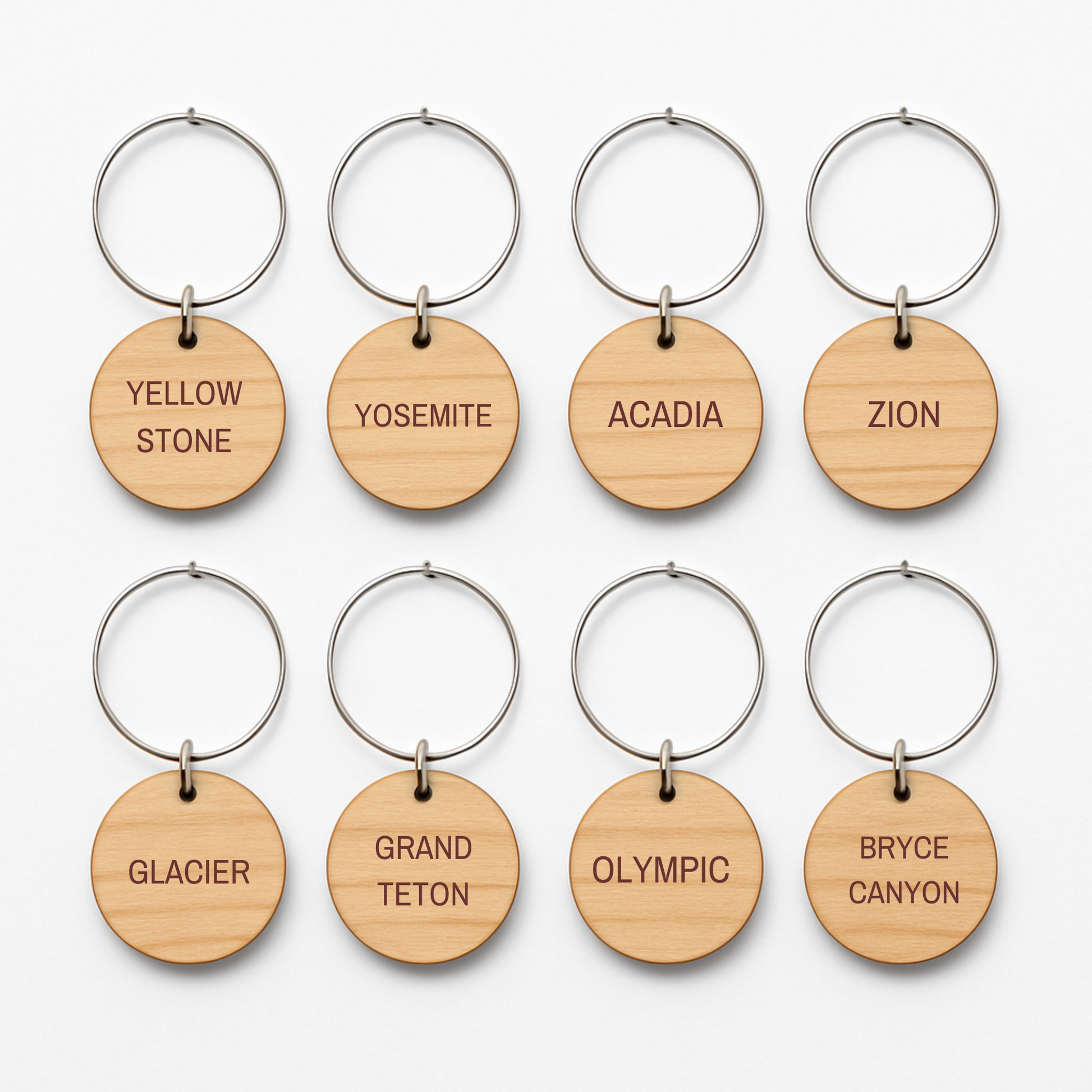 Eight round wooden keychains from Mirabilia Boutique's Awe-Inspiring National Parks Wine Charms are arranged in two rows, each engraved with a U.S. national park name—perfect for outdoor entertaining or as unique wine charms.