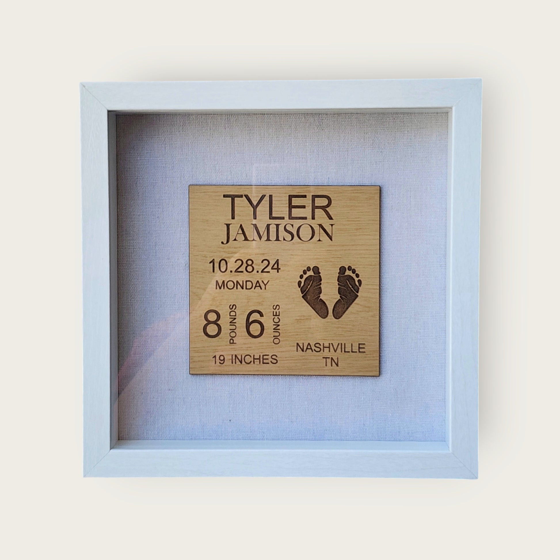 The "Baby Birth Stats Nursery Sign" by Mirabilia Boutique is a framed wooden plaque featuring engraved details such as "Tyler Jamison, 10.28.24, Monday, 8 pounds 6 ounces, 19 inches" and adorned with footprints. This personalized keepsake is perfect for a nursery in Nashville, TN.