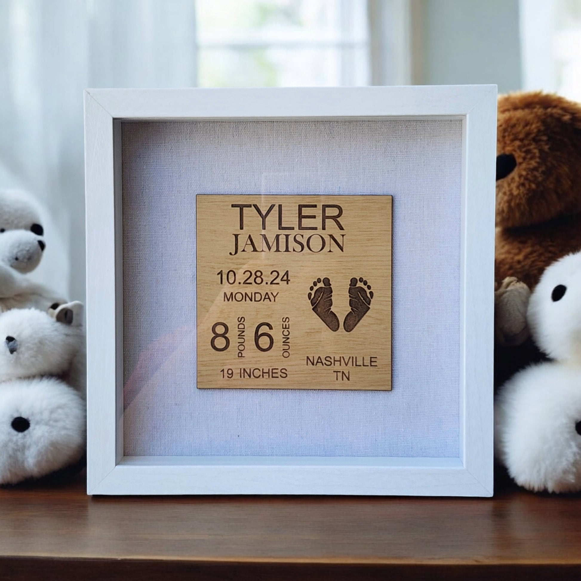 A white frame highlights Mirabilia Boutique's Baby Birth Stats Nursery Sign, featuring Tyler Jamison's name, birth date of October 28, 2024, weight of 8 pounds 6 ounces, length of 19 inches, location in Nashville TN, and charming footprints. This personalized keepsake is nestled among plush bears.