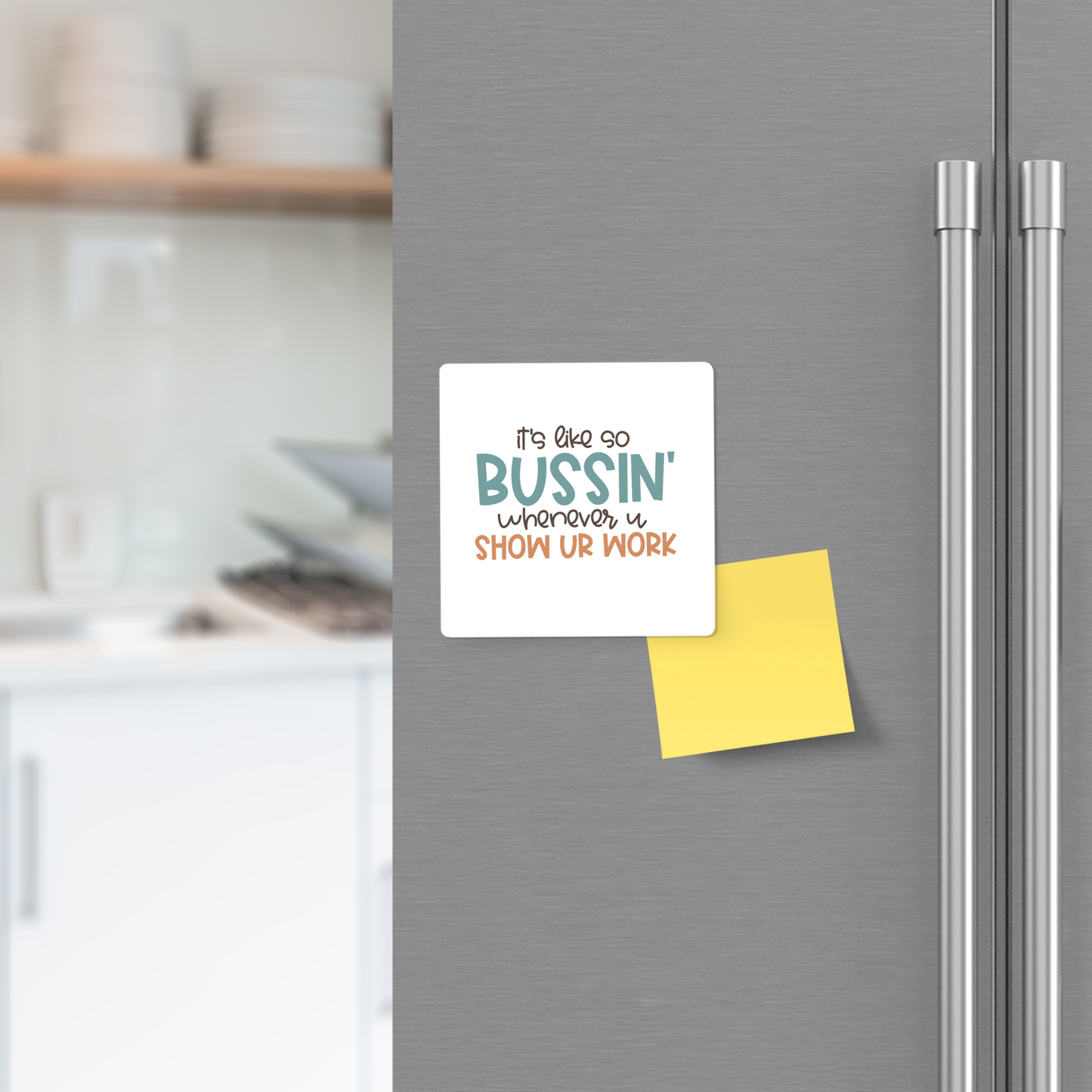 A fridge door displays the Mirabilia Boutique "It's So Bussin' Show Your Work" square magnet and a yellow sticky note below—perfect classroom decor or teacher gift. Blurred kitchen counter and shelves in the background.