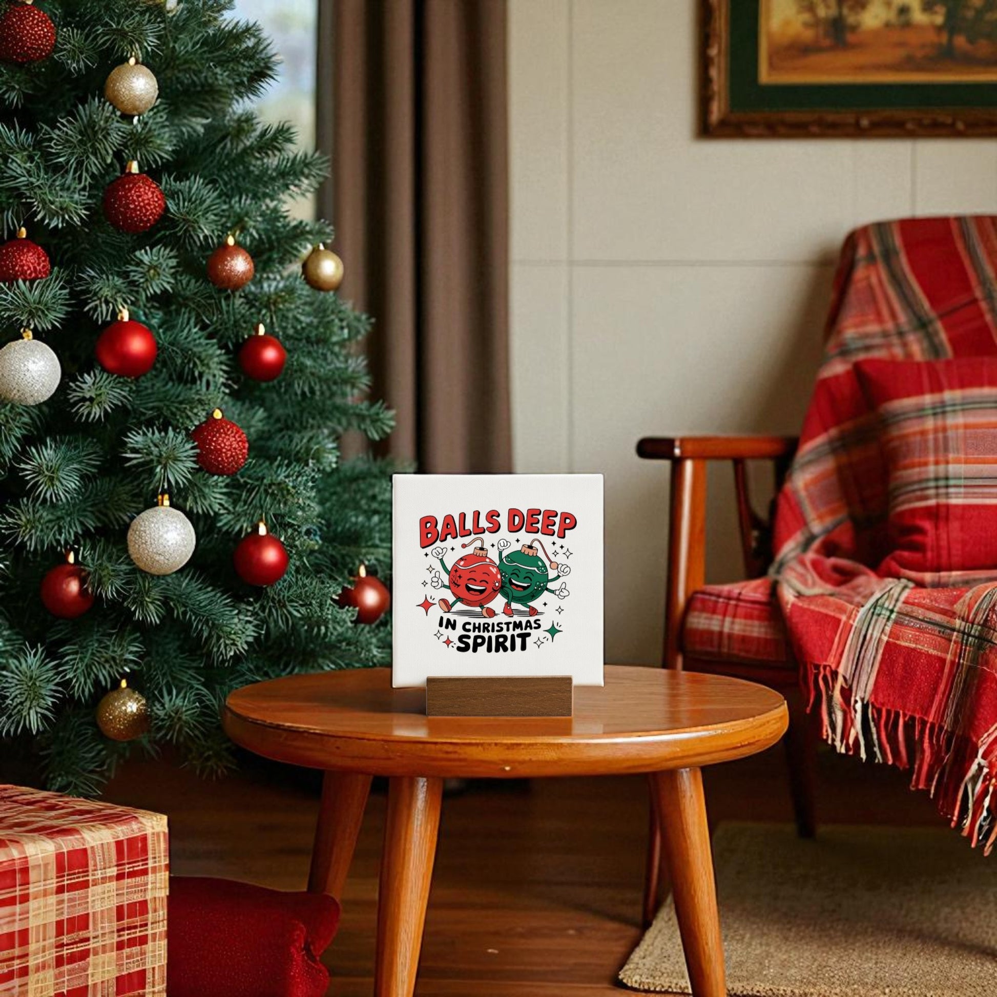 A decorated Christmas tree stands beside a cozy table featuring Mirabilia Boutique's "Balls Deep in Christmas Spirit" funny mini holiday sign. A red plaid blanket is draped over an armchair in the warmly lit living room.