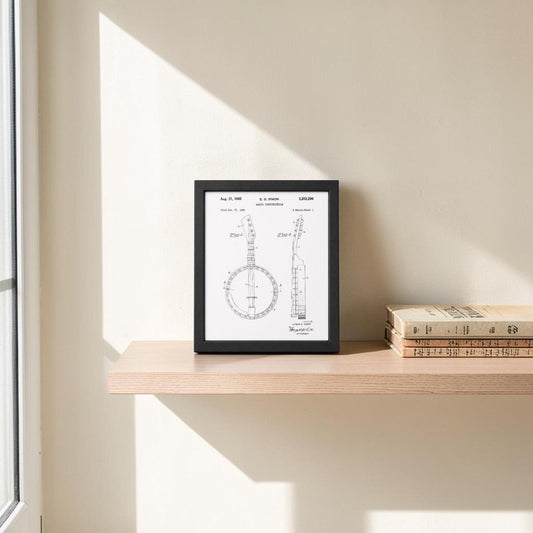 The Mirabilia Boutique Banjo Patent Print 8x10 Wall Art is displayed in a frame on a light wooden shelf beside three stacked books. Sunlight casts soft shadows on the beige wall, enhancing the vintage musical decor.