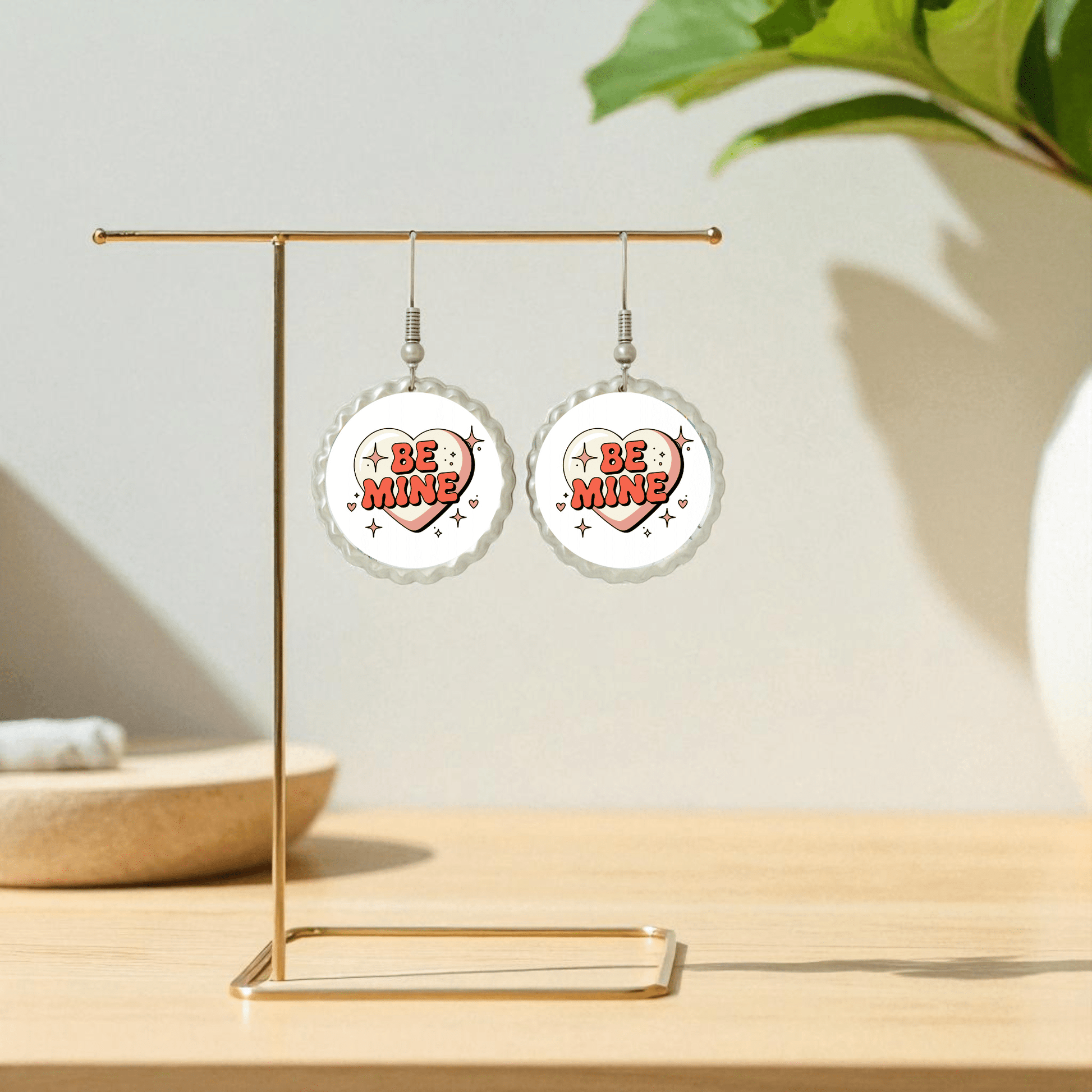The Be Mine Heart Earrings by Mirabilia Boutique feature retro heart designs with red "Be Mine" lettering, displayed on a gold stand—perfect as a cute Valentine jewelry gift.