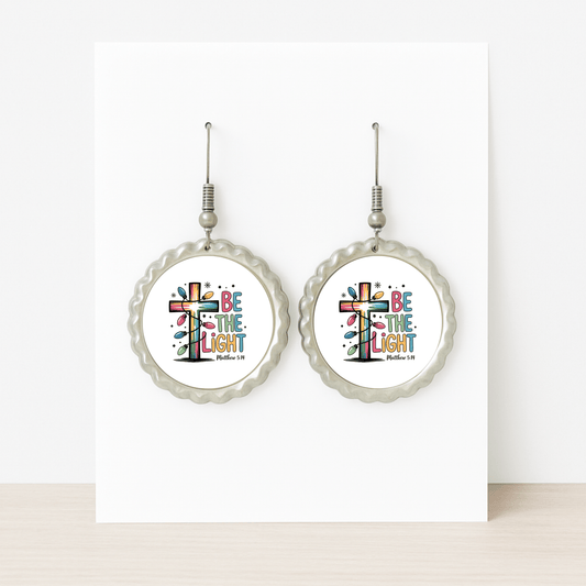 A pair of "Be the Light" earrings by Mirabilia Boutique featuring a colorful cross and Matthew 5:14—Christian gifts displayed on a card with scalloped silver edges, perfect for faith-inspired giving.