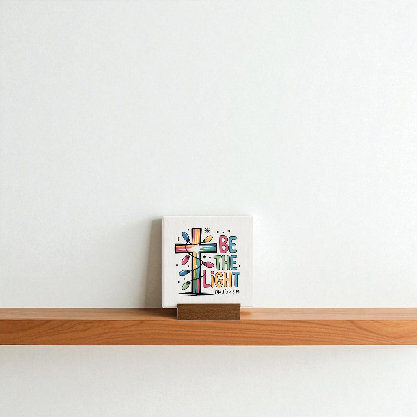 The Be the Light Mini Sign | Christian Christmas Decor 4x4 by Mirabilia Boutique adds a colorful, inspirational touch to any shelf—ideal as a Christian gift or festive accent for a plain white wall.