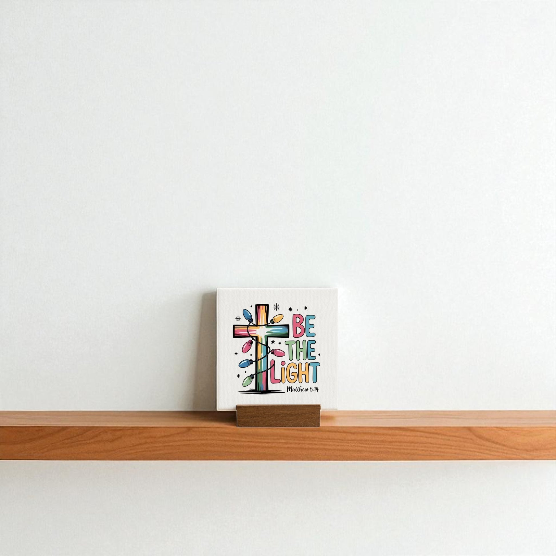The Be the Light Mini Sign | Christian Christmas Decor 4x4 by Mirabilia Boutique adds a colorful, inspirational touch to any shelf—ideal as a Christian gift or festive accent for a plain white wall.