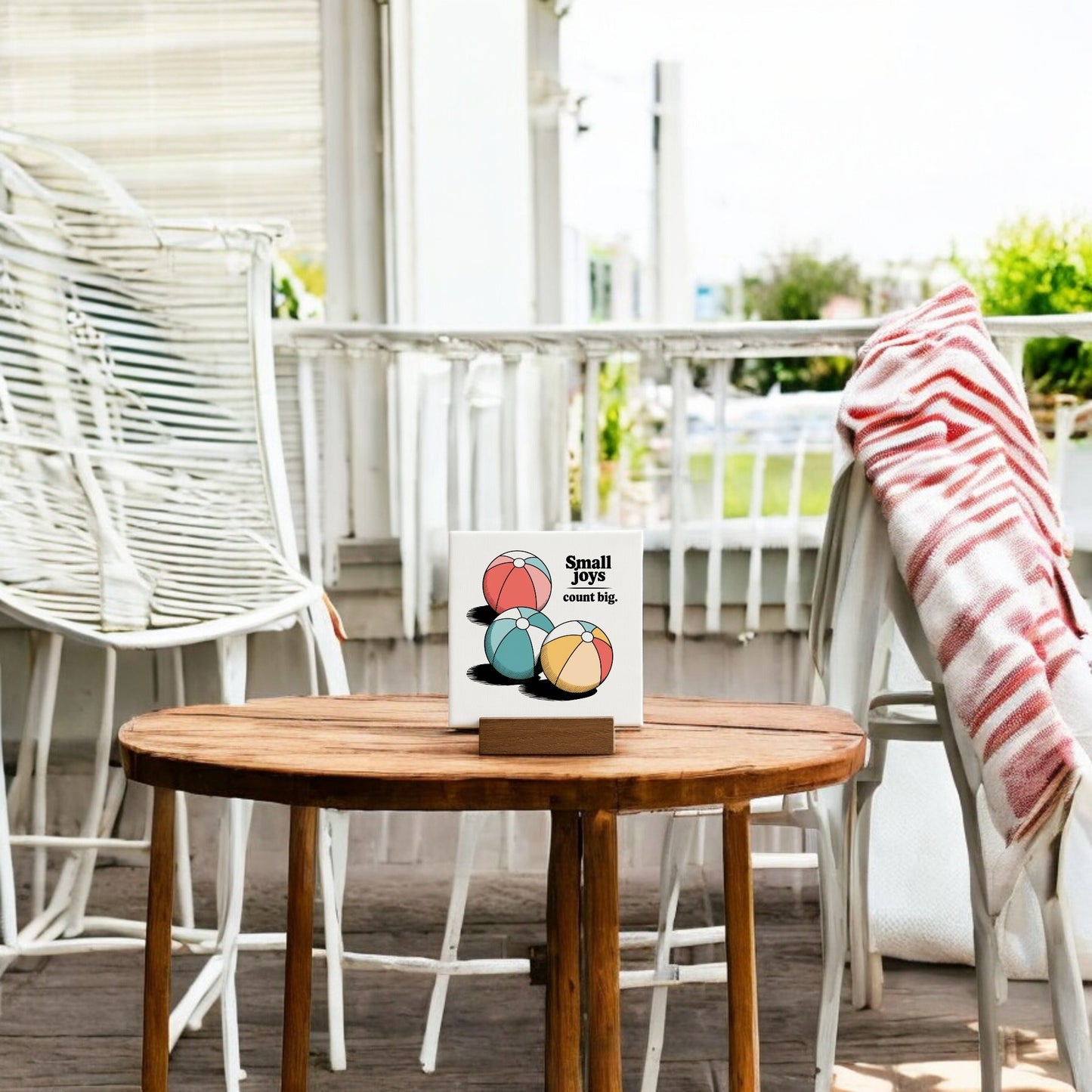 A table with chairs, a towel, and the Mirabilia Boutique Small Joys Count Big Mini Canvas – 4x4 Summer Desk Sign are perfect touches for relaxed summer home decor.