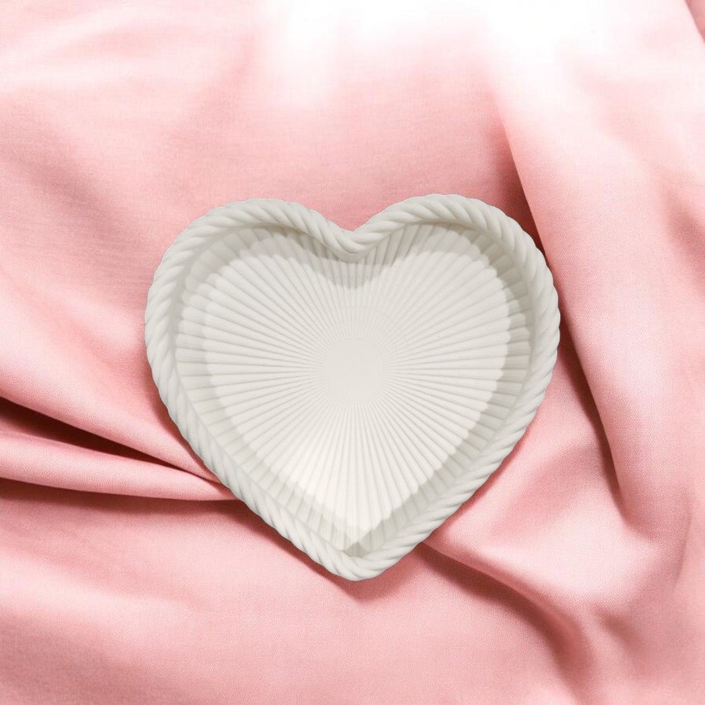 The Coastal Heart Tray in Matte White by Mirabilia Boutique features a heart shape, ridged design, and rope-like border—resting on soft pink fabric, it’s perfect for beach-inspired decor.