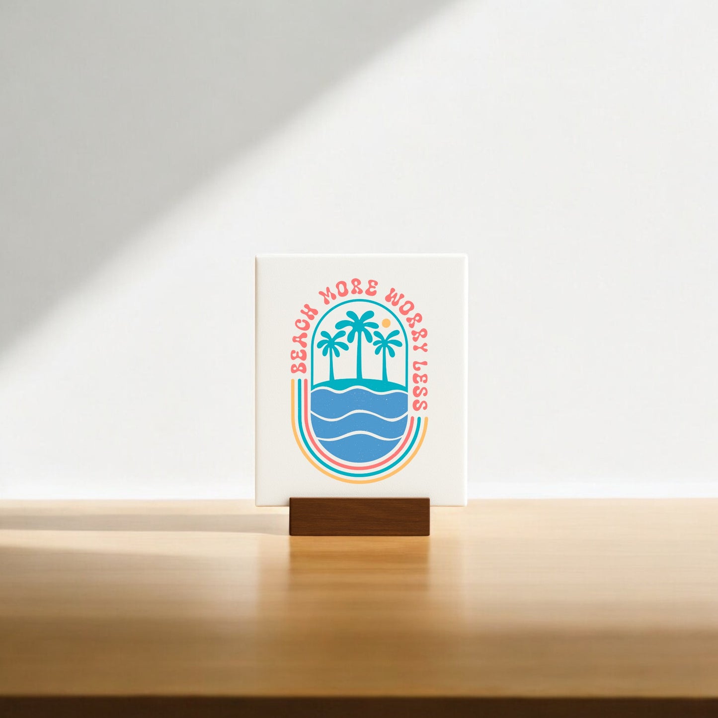 The Mirabilia Boutique "Beach More Worry Less Retro Summer Sign" features palm trees over waves in colorful retro style on a wooden stand—ideal as beach decor or a fun summer gift. Sunlight casts a soft shadow for added charm.