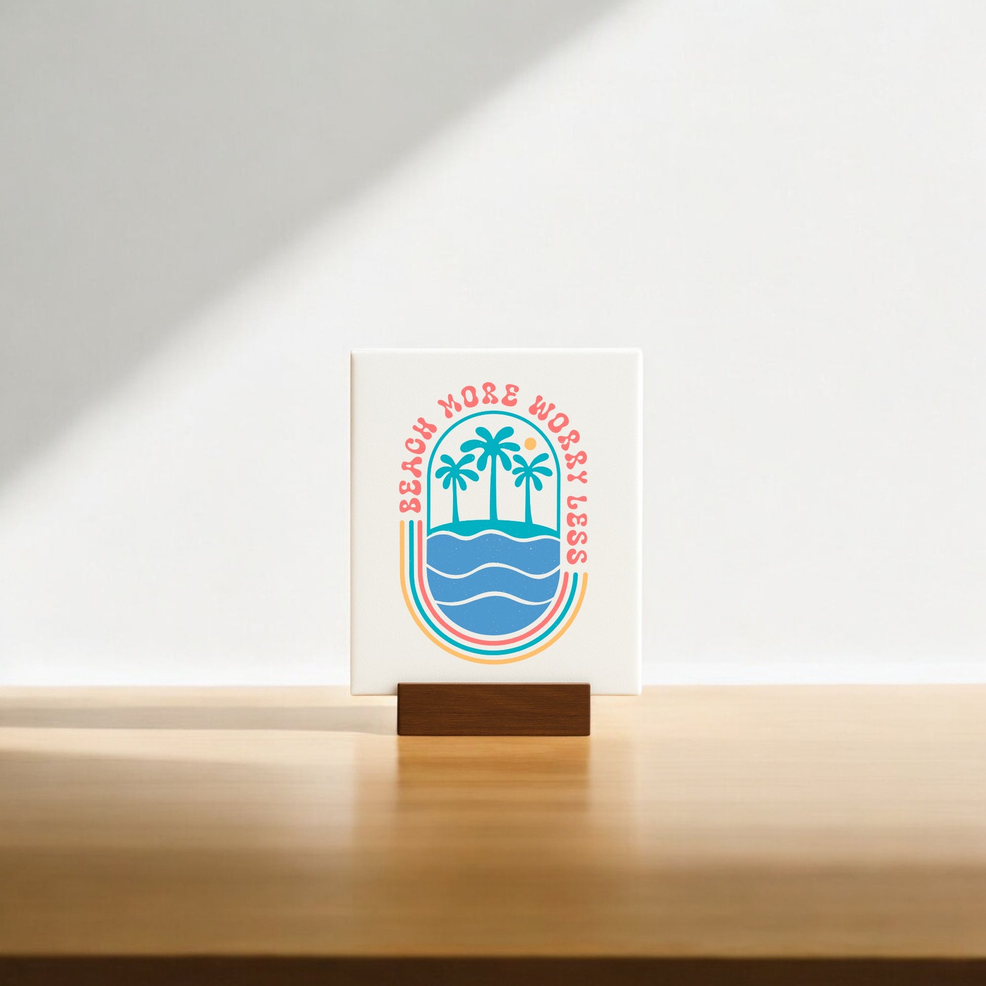 The Mirabilia Boutique "Beach More Worry Less Retro Summer Sign" features palm trees over waves in colorful retro style on a wooden stand—ideal as beach decor or a fun summer gift. Sunlight casts a soft shadow for added charm.