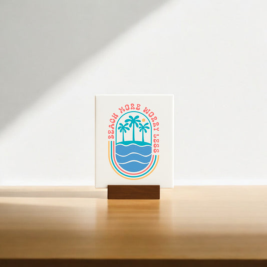 The Mirabilia Boutique "Beach More Worry Less Retro Summer Sign" features palm trees over waves in colorful retro style on a wooden stand—ideal as beach decor or a fun summer gift. Sunlight casts a soft shadow for added charm.