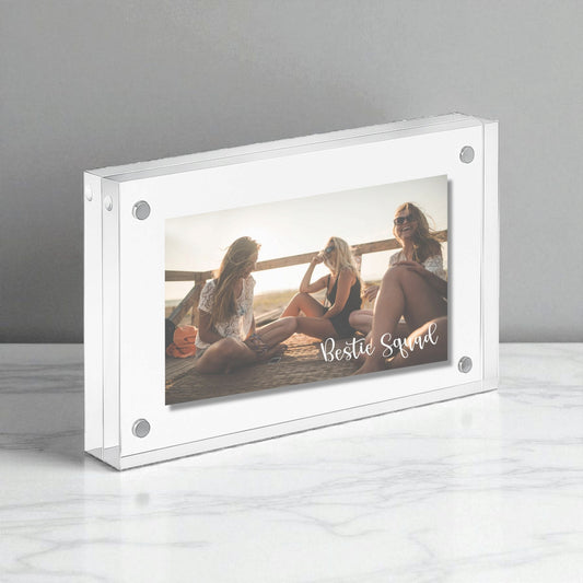 The Mirabilia Boutique Bestie Squad Acrylic Frame displays a 5x7 photo on a white marble surface, featuring “Bestie Squad” and capturing three women enjoying friendship in the sunlight.