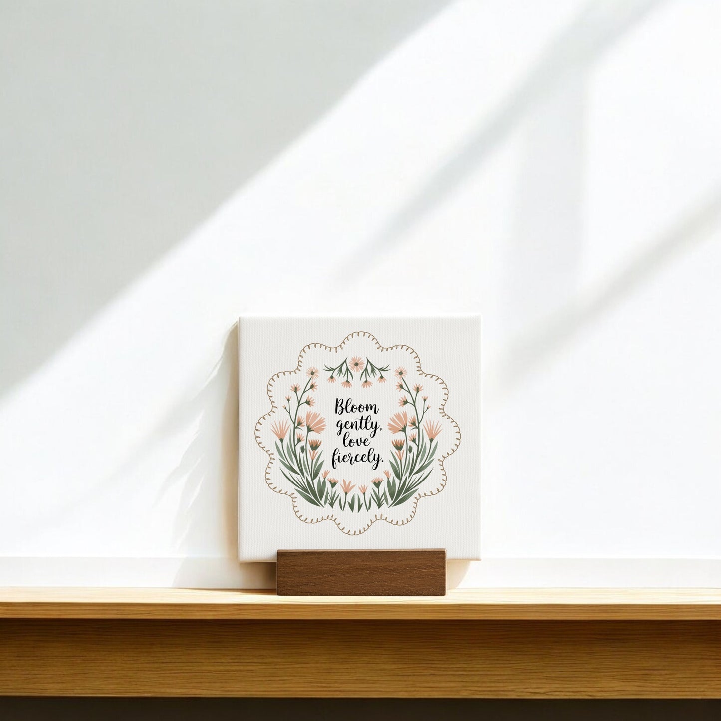 The Bloom Gently Love Fiercely Mini Canvas Sign by Mirabilia Boutique features floral artwork and an uplifting phrase, displayed on a wooden stand as wildflower decor—perfect as an inspiring encouragement gift.