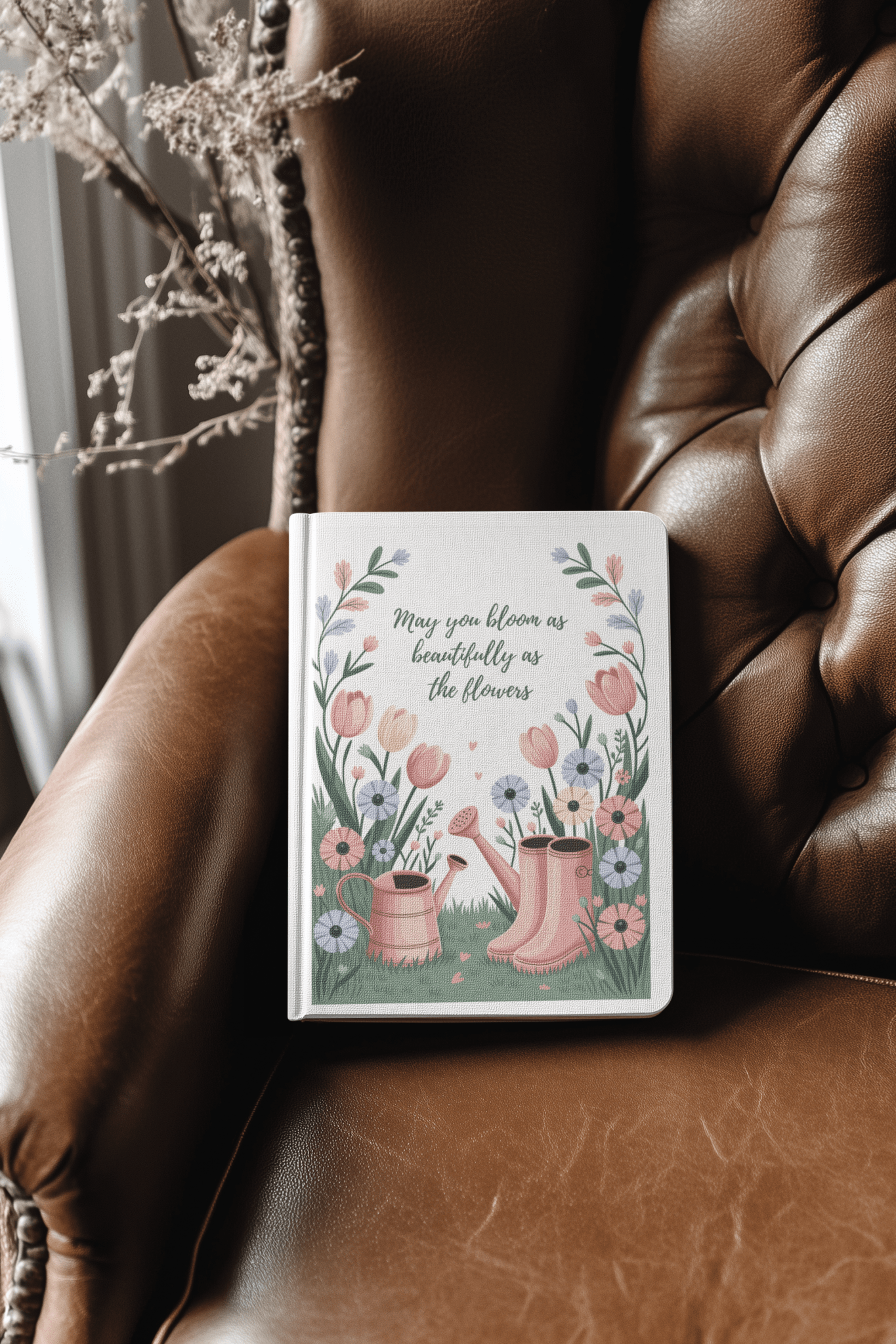 The Bloom Like the Flowers Journal – A5 Spring Floral Notebook by Mirabilia Boutique features a floral cover with pink boots on a brown leather chair and the quote, "May you bloom as beautifully as the flowers"—a perfect gift for garden lovers.