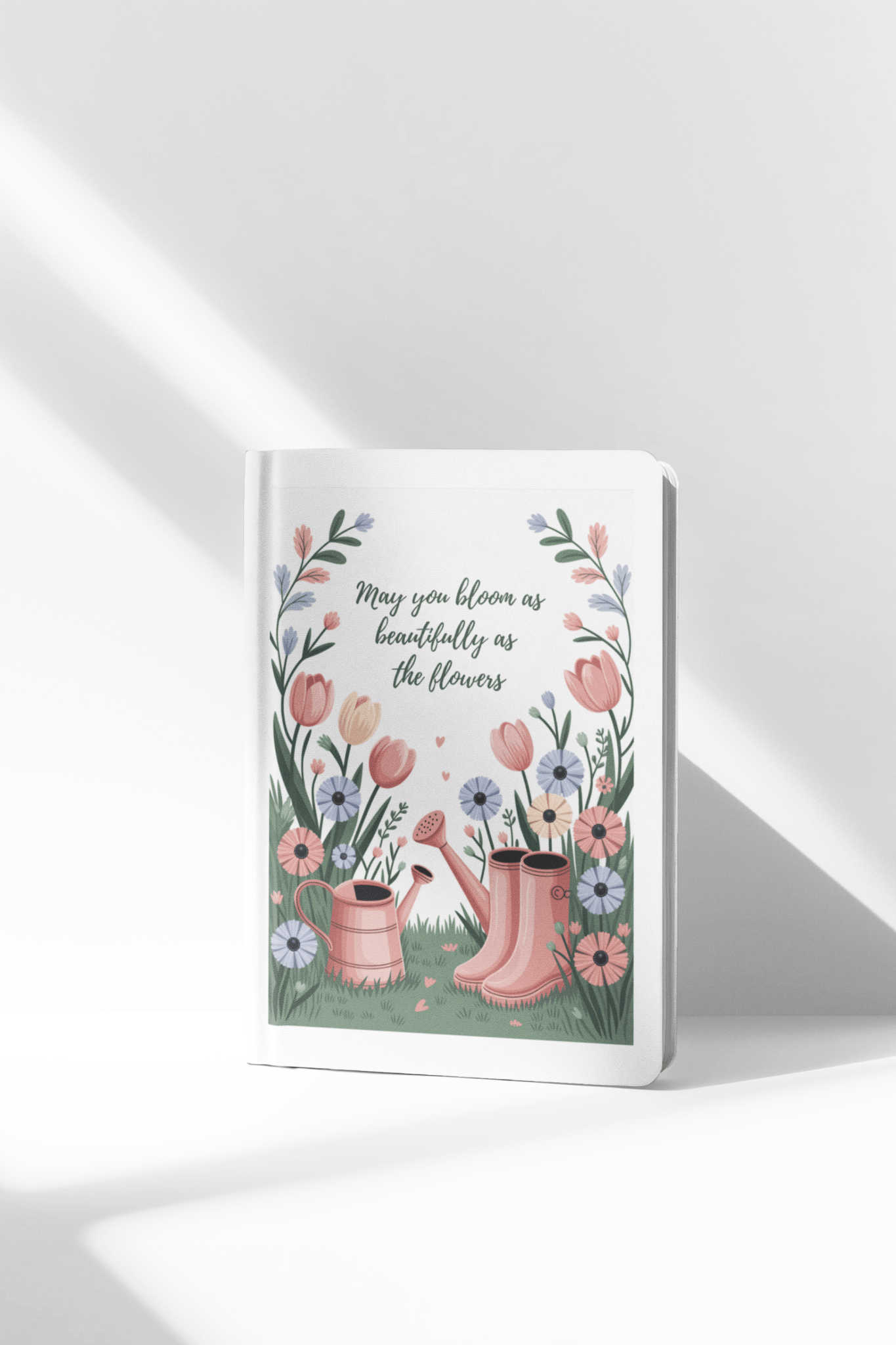The Bloom Like the Flowers Journal – A5 Spring Floral Notebook by Mirabilia Boutique features an illustrated cover with pink boots, a watering can, and vibrant flowers, plus the quote, "May you bloom as beautifully as the flowers." Ideal for garden lovers.