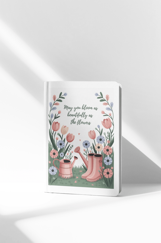The Bloom Like the Flowers Journal – A5 Spring Floral Notebook by Mirabilia Boutique features an illustrated cover with pink boots, a watering can, and vibrant flowers, plus the quote, "May you bloom as beautifully as the flowers." Ideal for garden lovers.