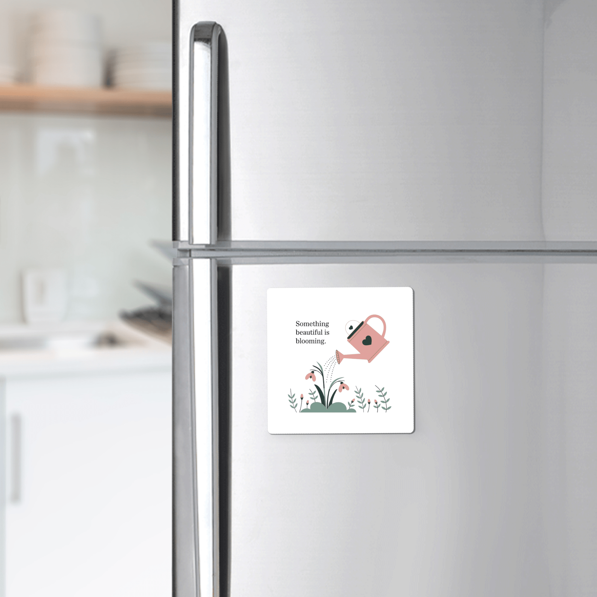 A white fridge displays the Mirabilia Boutique "Something Beautiful Is Blooming" magnet—growth-inspired decor with a pink watering can, flowers, and uplifting text. A thoughtful self-care gift and gentle mental health reminder. Kitchen counter in background.