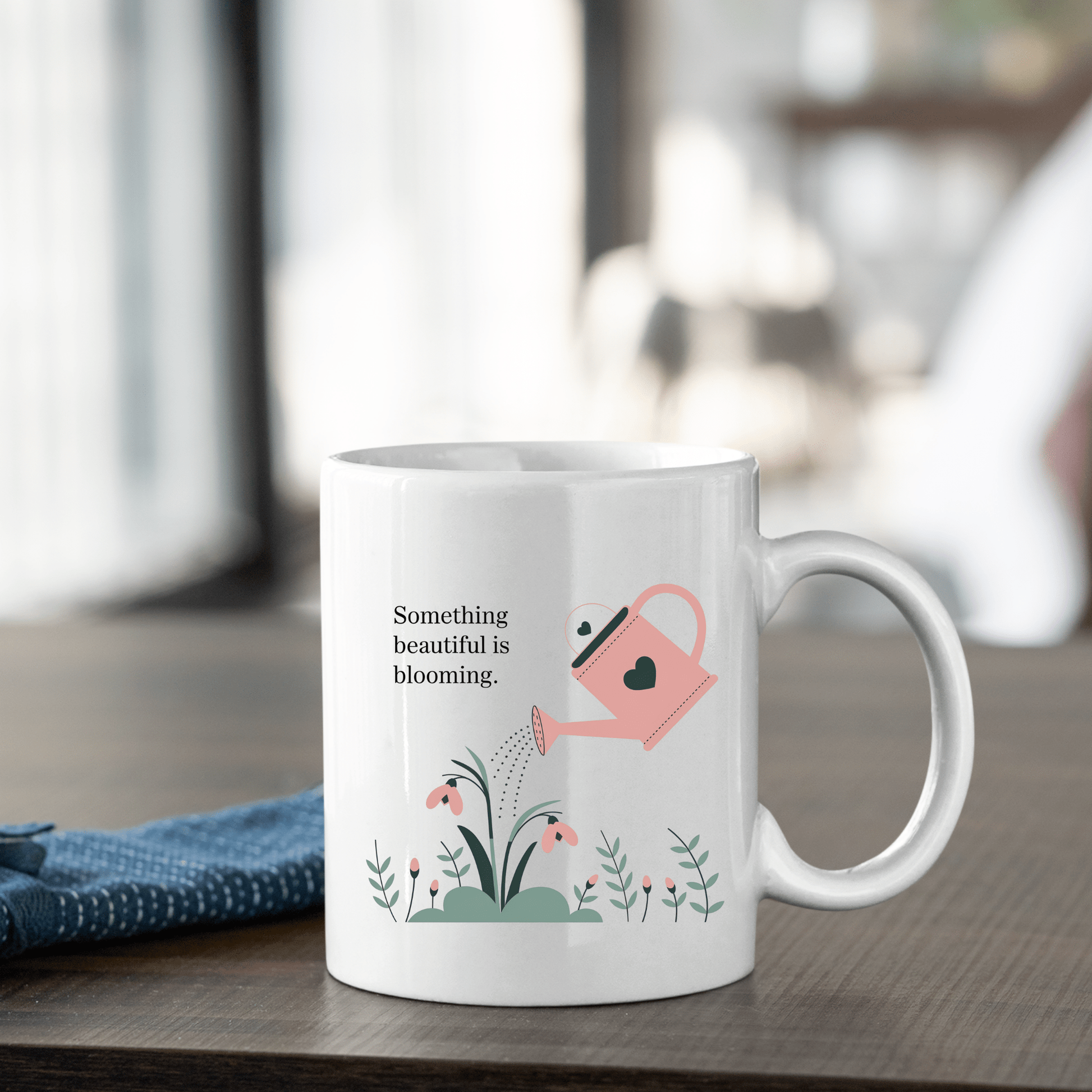The Something Beautiful Is Blooming Mug by Mirabilia Boutique features a white design with a pink watering can, floral green plants, and the message "Something beautiful is blooming"—a perfect growth and positivity gift.