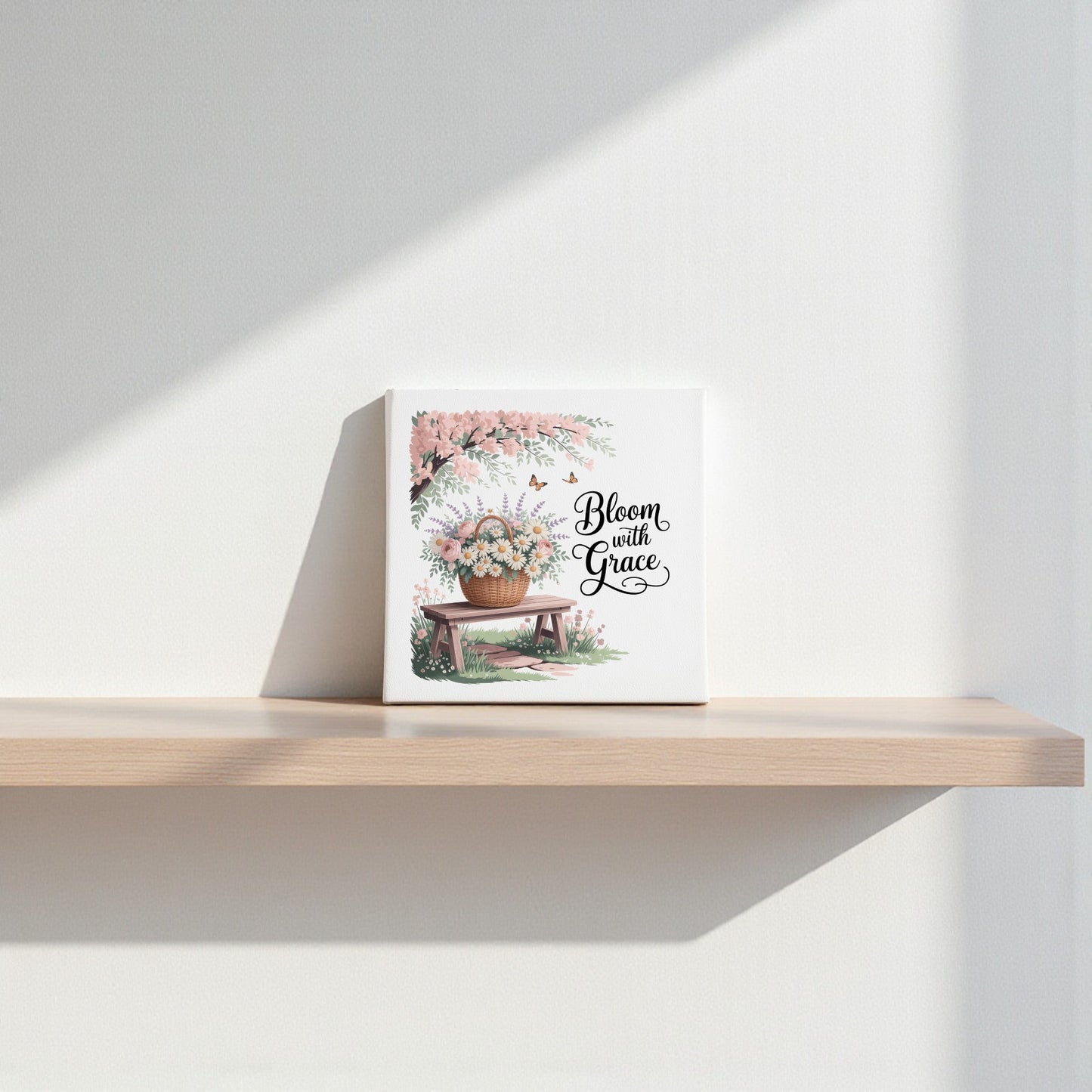 The Bloom with Grace Floral Canvas Wall Art by Mirabilia Boutique, featuring floral artwork and an inspiring quote, is displayed on a light wooden shelf and softly illuminated against a white wall.