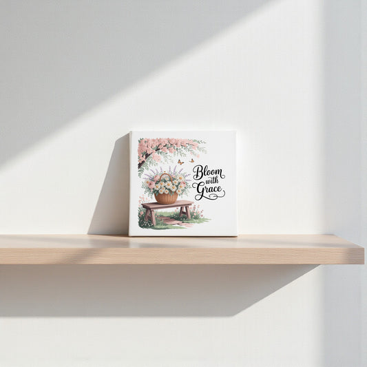 The Bloom with Grace Floral Canvas Wall Art by Mirabilia Boutique, featuring floral artwork and an inspiring quote, is displayed on a light wooden shelf and softly illuminated against a white wall.
