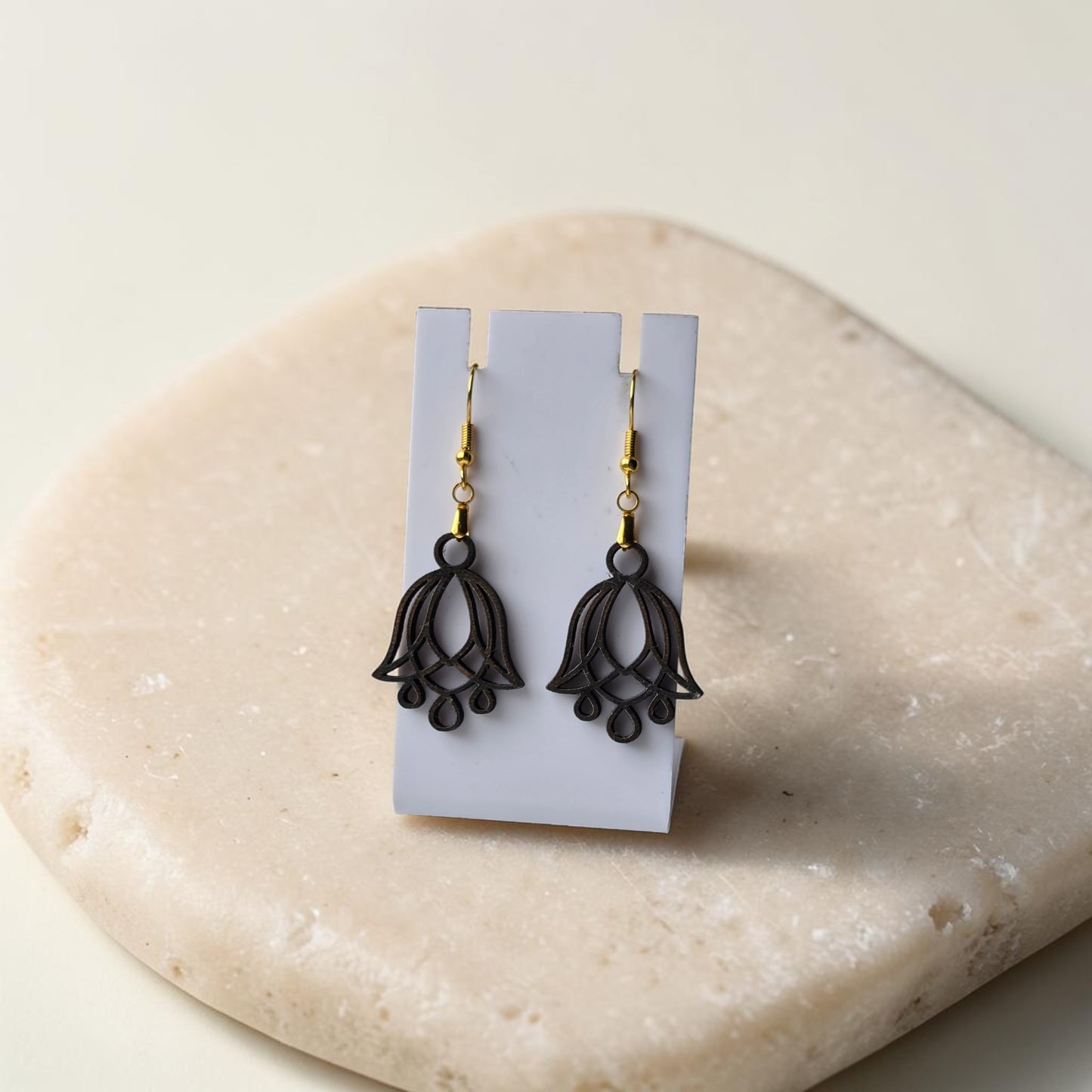 Bluebell Flower Earrings by Mirabilia Boutique, crafted from lasercut walnut wood with a delicate floral design, displayed on a white stand atop a smooth beige stone surface.