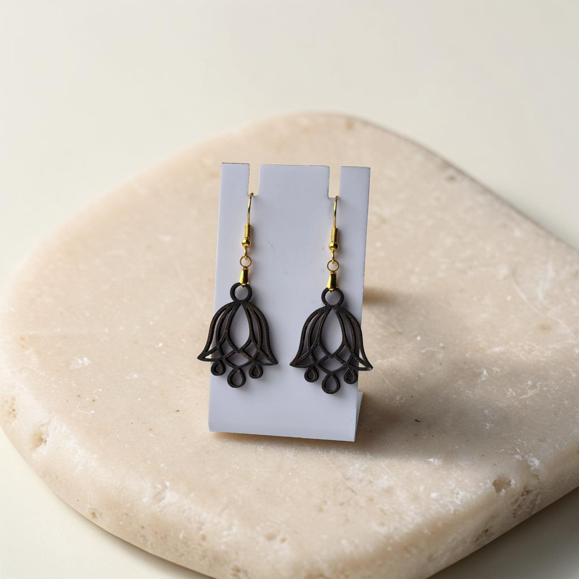 Bluebell Flower Earrings by Mirabilia Boutique, crafted from lasercut walnut wood with a delicate floral design, displayed on a white stand atop a smooth beige stone surface.